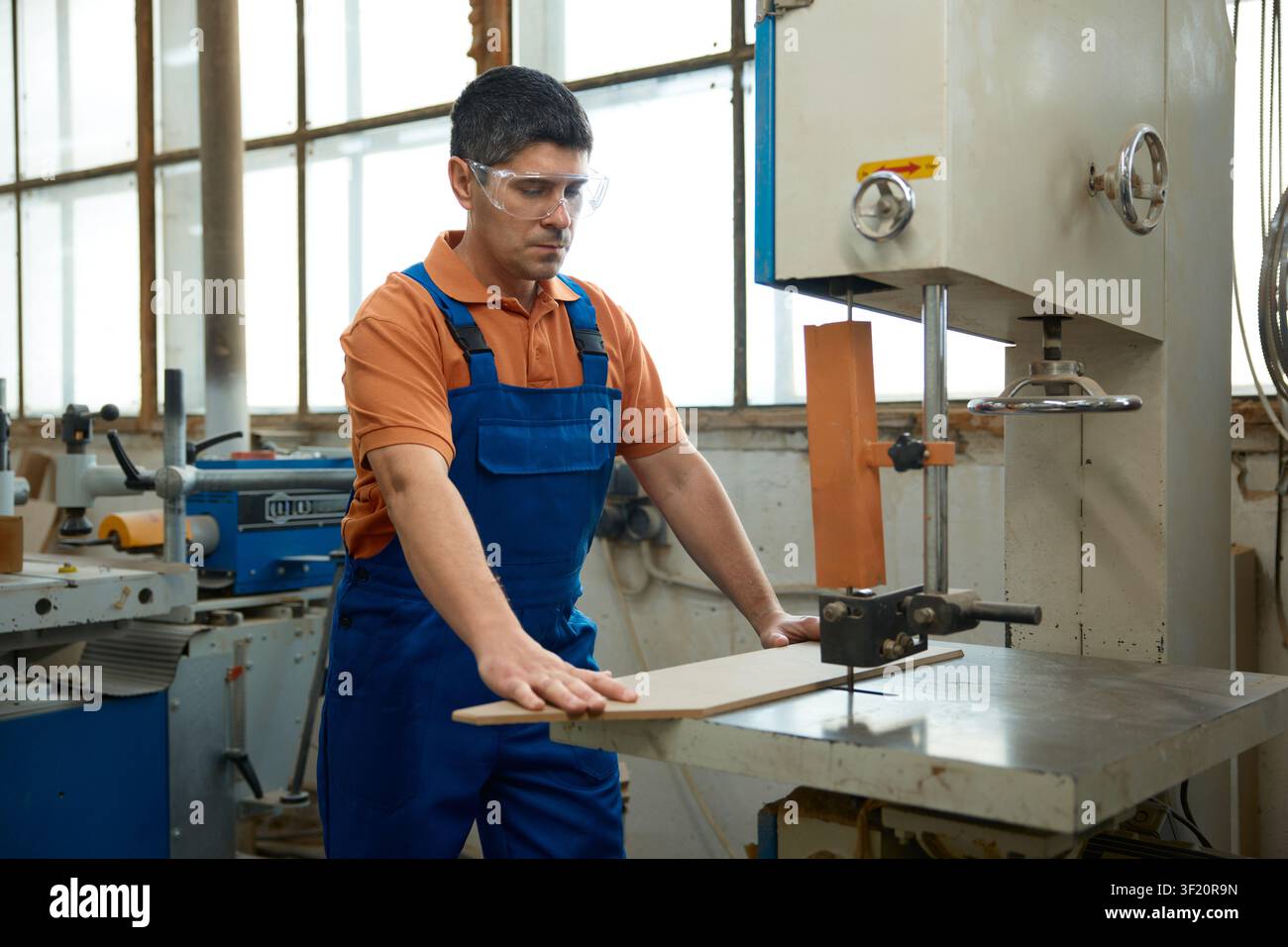 Skilled carpenter using bandsaw to shape curved panel while maintaining safety precautions and focus Stock Photo