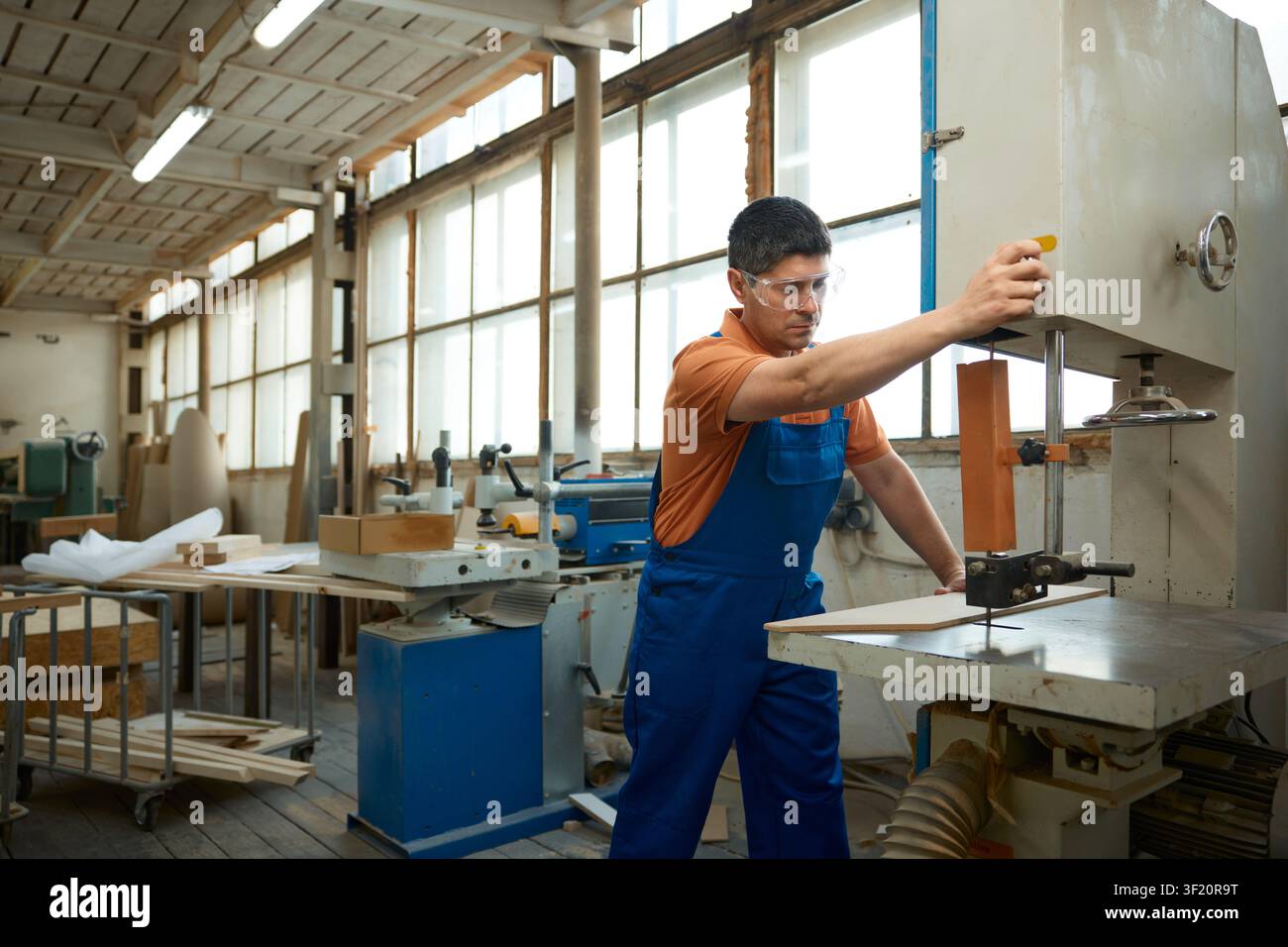 Skilled carpenter using bandsaw to shape curved panel while maintaining safety precautions and focus Stock Photo