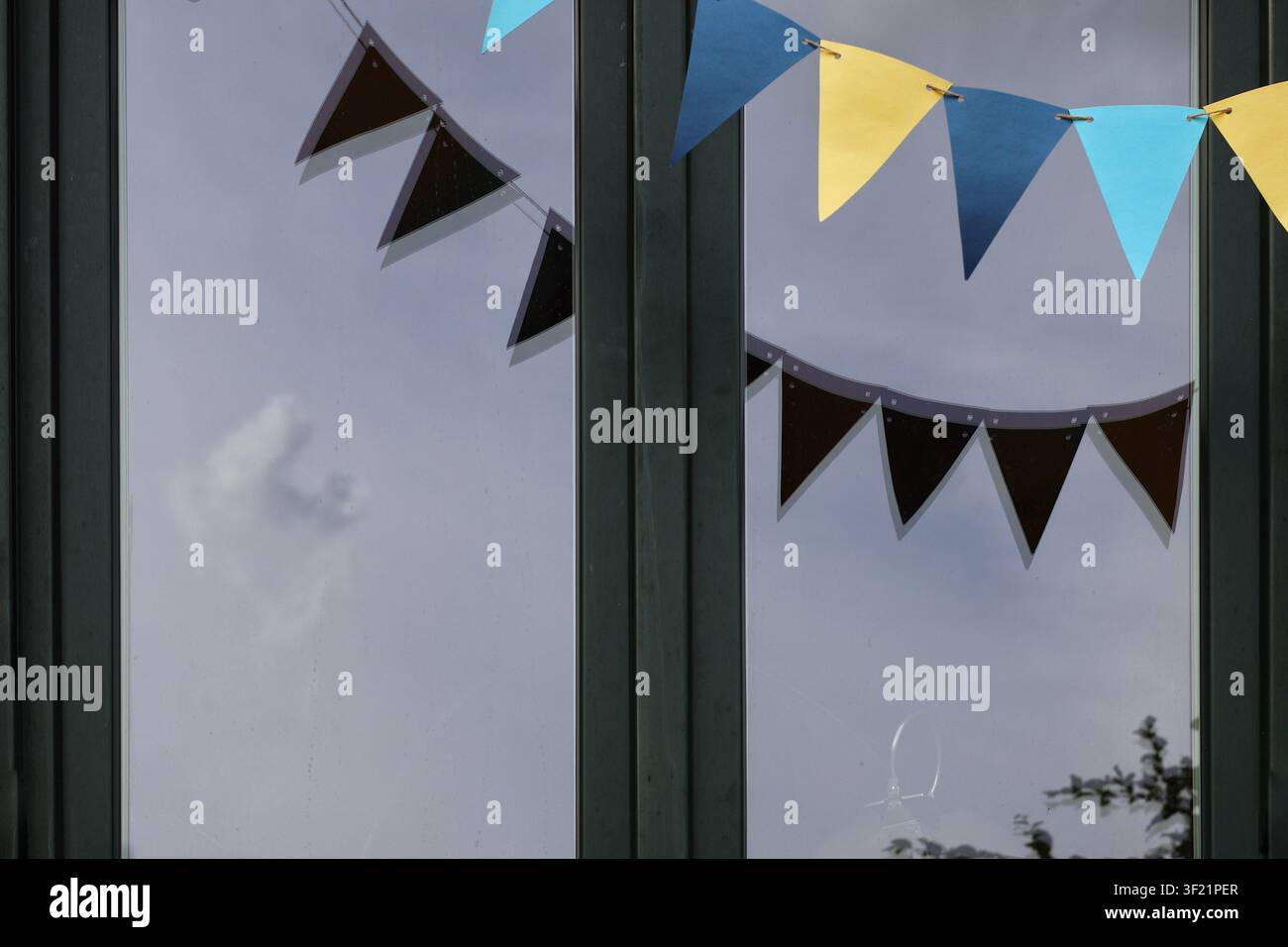 Colorful Bunting Reflected in Modern Glass Window with Cloudy Sky – Festive Abstract Architectural Detail Stock Photo
