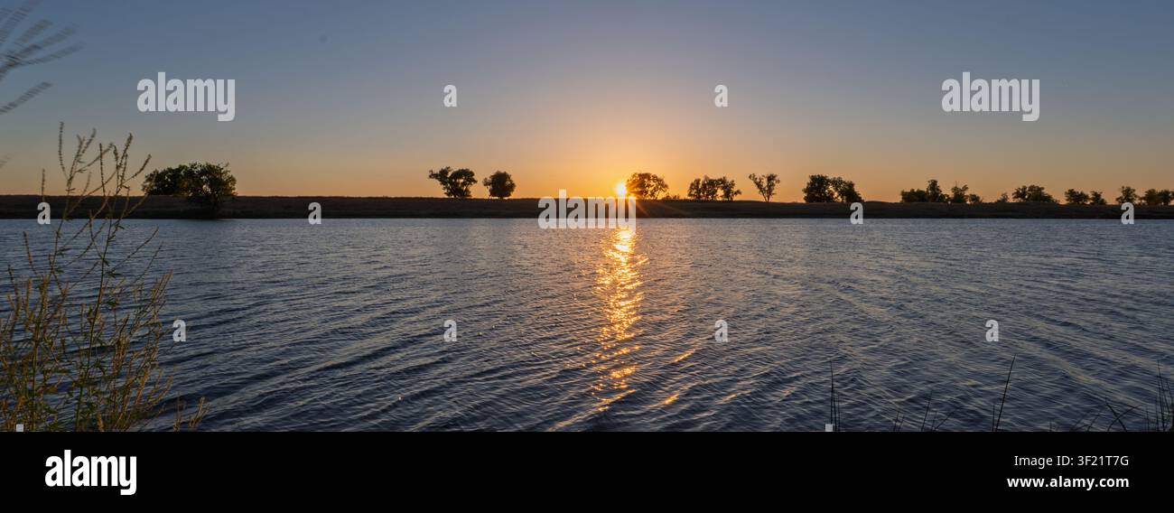 Panoramic sunset over a tranquil, deep blue river Stock Photo
