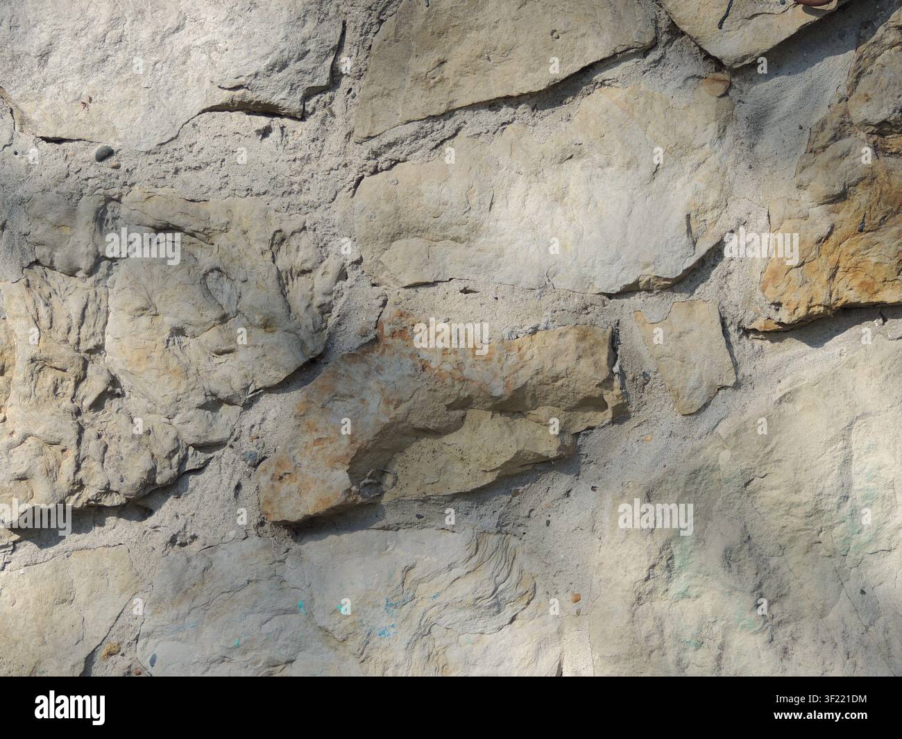 wall of large, uncut, light-colored stones, bonded with cement mortar. The surface has a rough, textured, chipped surface, casting a soft shadow Stock Photo