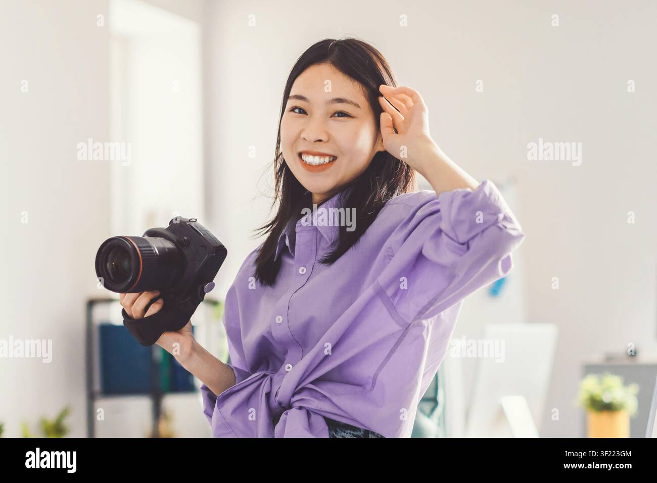 Smiling Asian Woman Holding Camera In Modern Office, Photography Concept Stock Photo