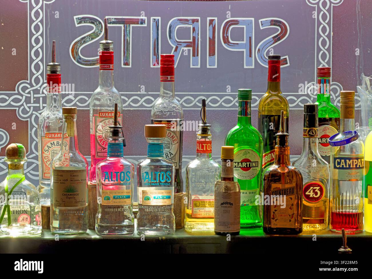 Colourful spirits bottles fill a window at the Lass O'Gowrie pub in Manchester as younger drinkers increasingly explore low and no-alcohol choices Stock Photo