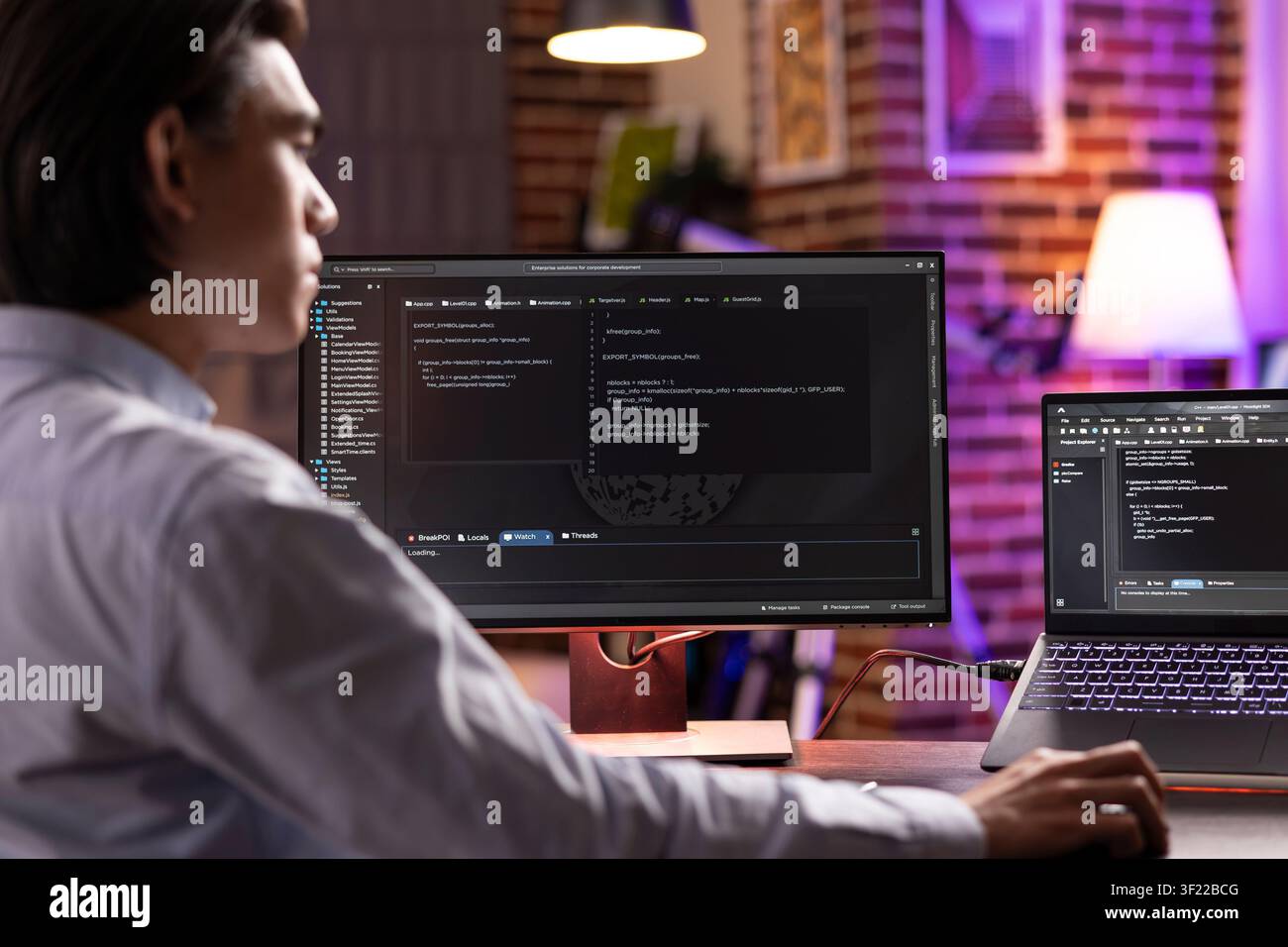 Male remote worker using digital devices in completing programming projects late at night. Asian entrepreneur studying and debugging coding scripts, ensuring functioning website for potential client. Stock Photo