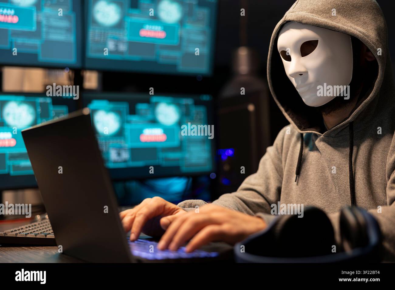 Masked hacker attempts data breach, targeting sensitive digital information in tech environment. Freelance programmer anonymously writes malware code on laptop, hacking into system software. Stock Photo