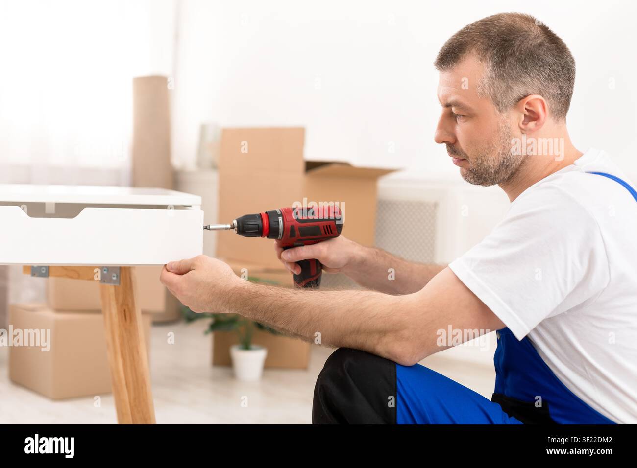 Side-View Of Carpenter Man Assembling Table Using Electric Drill Indoors Stock Photo