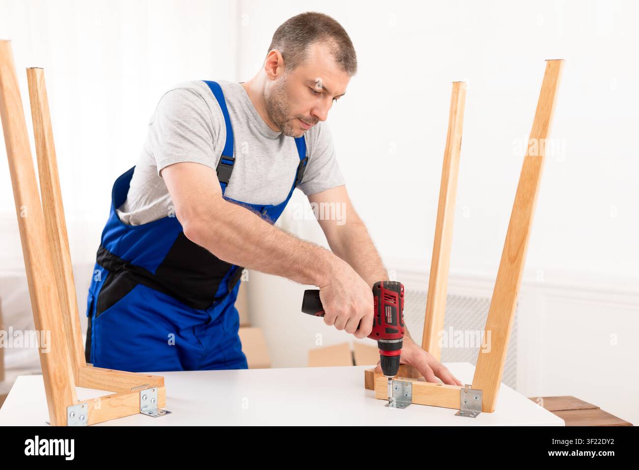 Male Carpenter Using Electric Drill Assembling Wooden Table In Studio Stock Photo