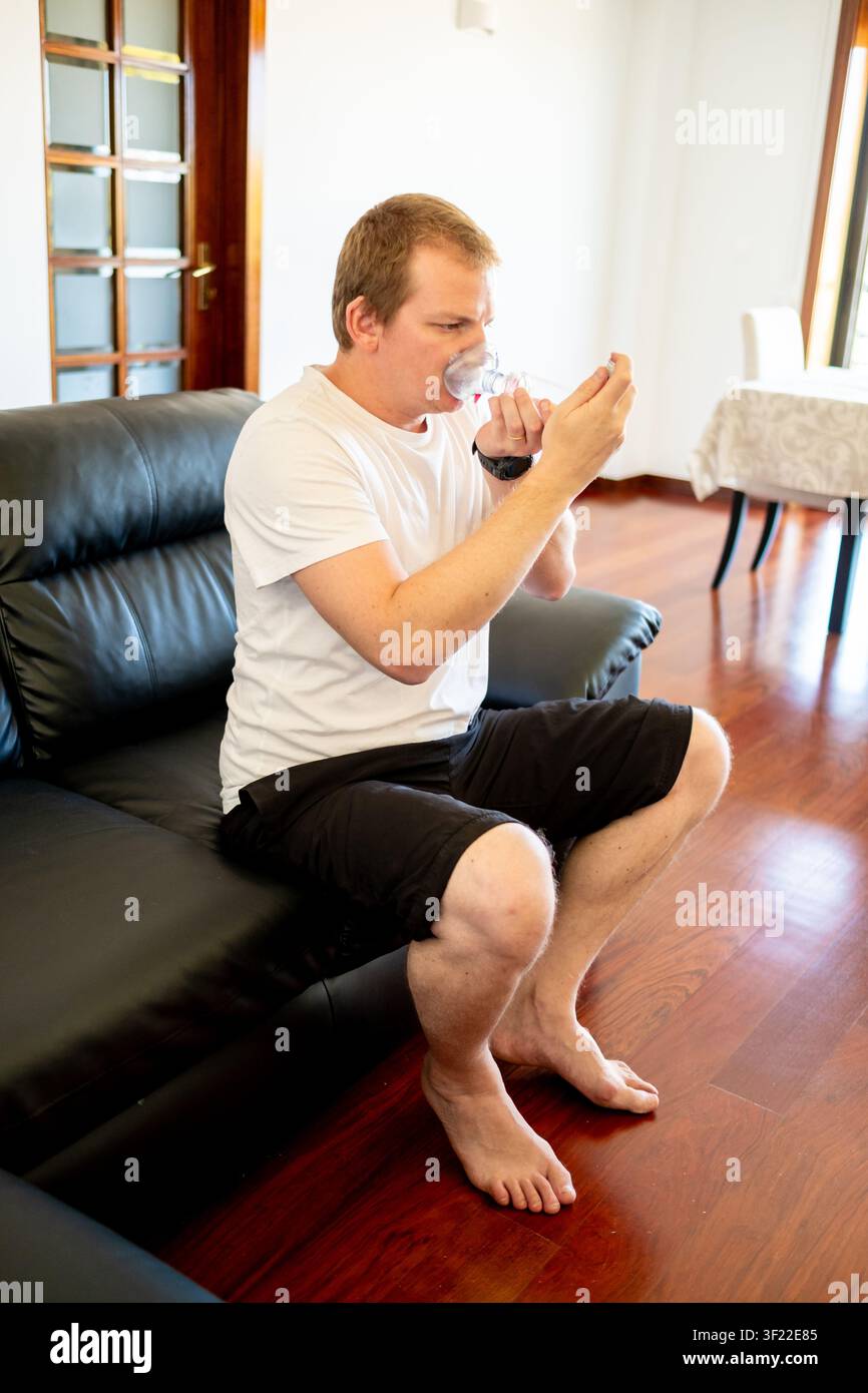 Man managing asthma at home, using an inhaler and spacer for respiratory health Stock Photo