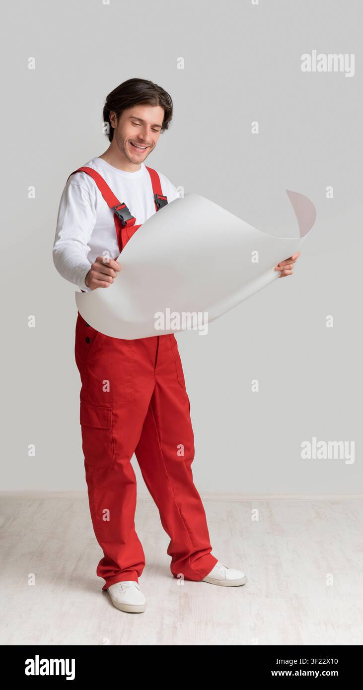 Repairment Plan. Smiling Young Engineer Holding Blueprint, Checking Project Details Stock Photo