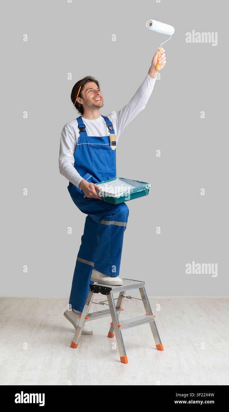 Painting Services Concept. Worker Holding Paint Roller, Applying Dye To Ceiling Stock Photo