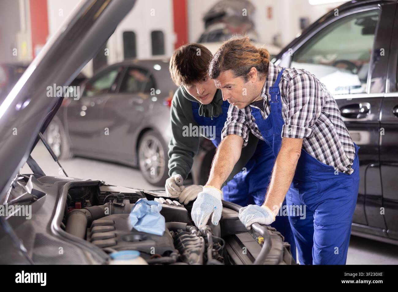 Two mechanics examining car engine under open hood in workshop Stock Photo