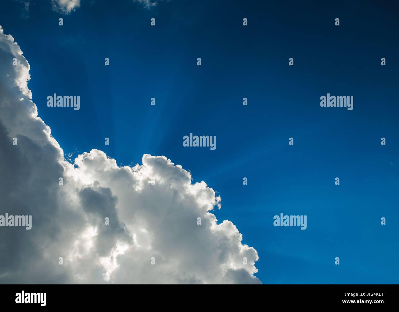 Dramatic blue sky with sun rays shining through fluffy white clouds Stock Photo