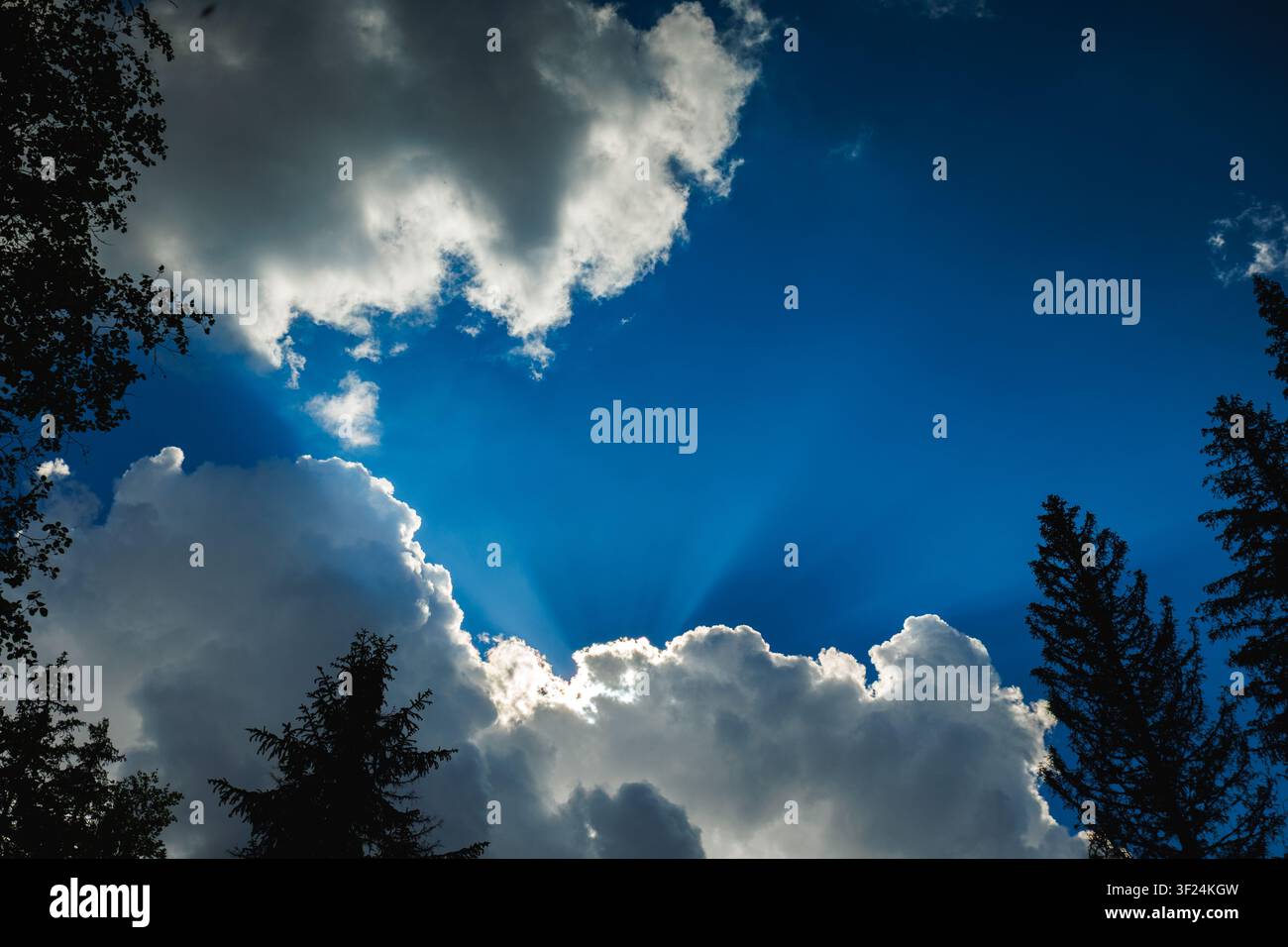 Dramatic blue sky with sun rays shining through fluffy white clouds Stock Photo