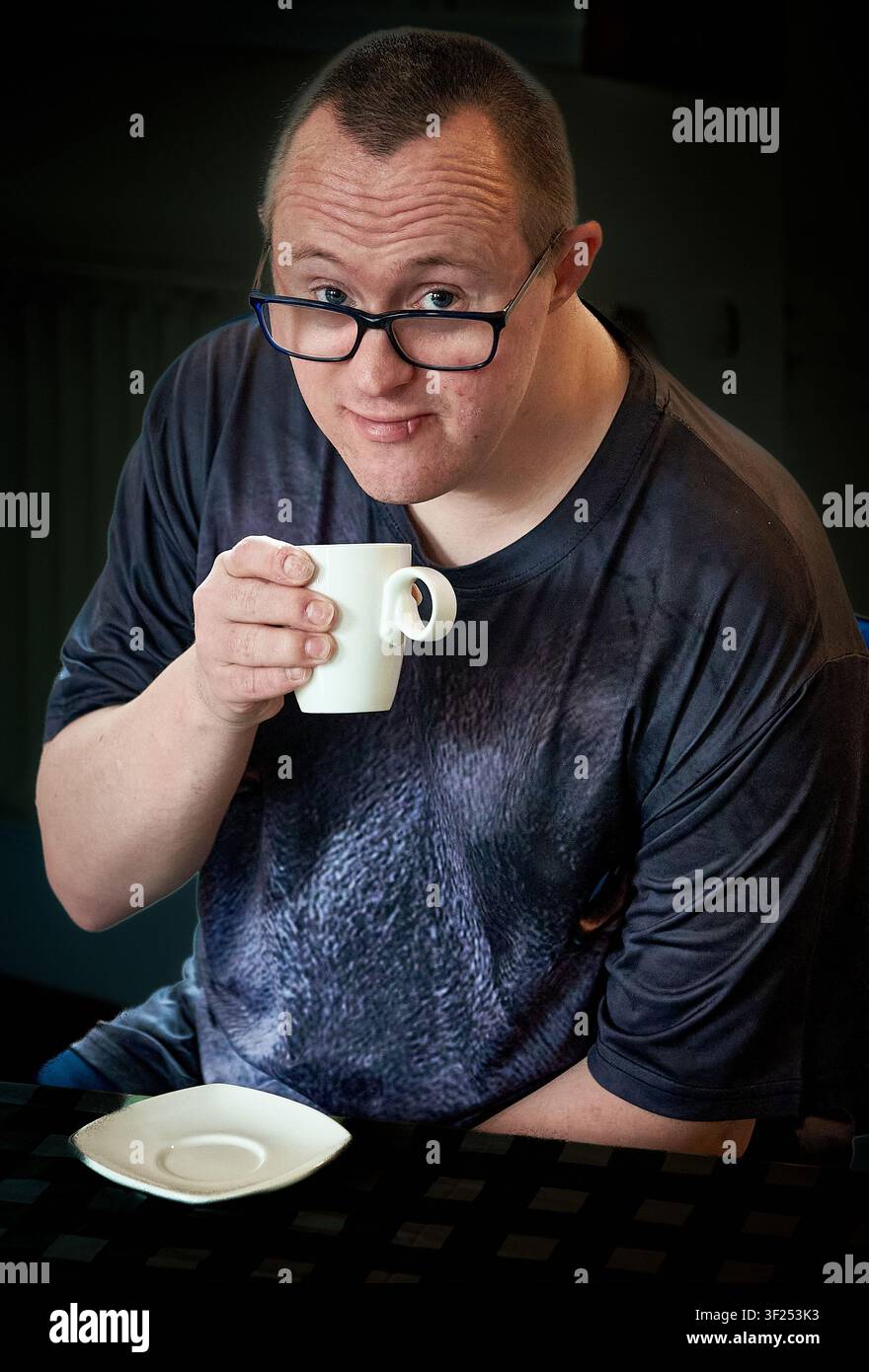 Portrait of a young man with Down syndrome holding a cup of coffee and smiling at the camera, UK Stock Photo
