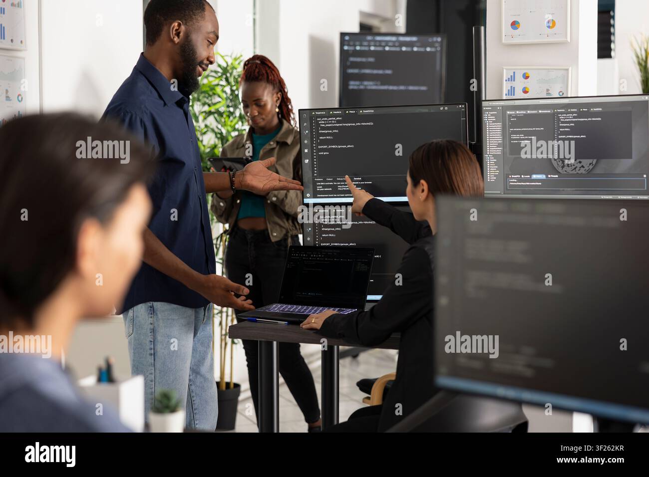 Male and female developers review software data, improving app functionality and company website performance. Diverse coders analyzing HTML scripts on laptop and desktop monitors. Stock Photo