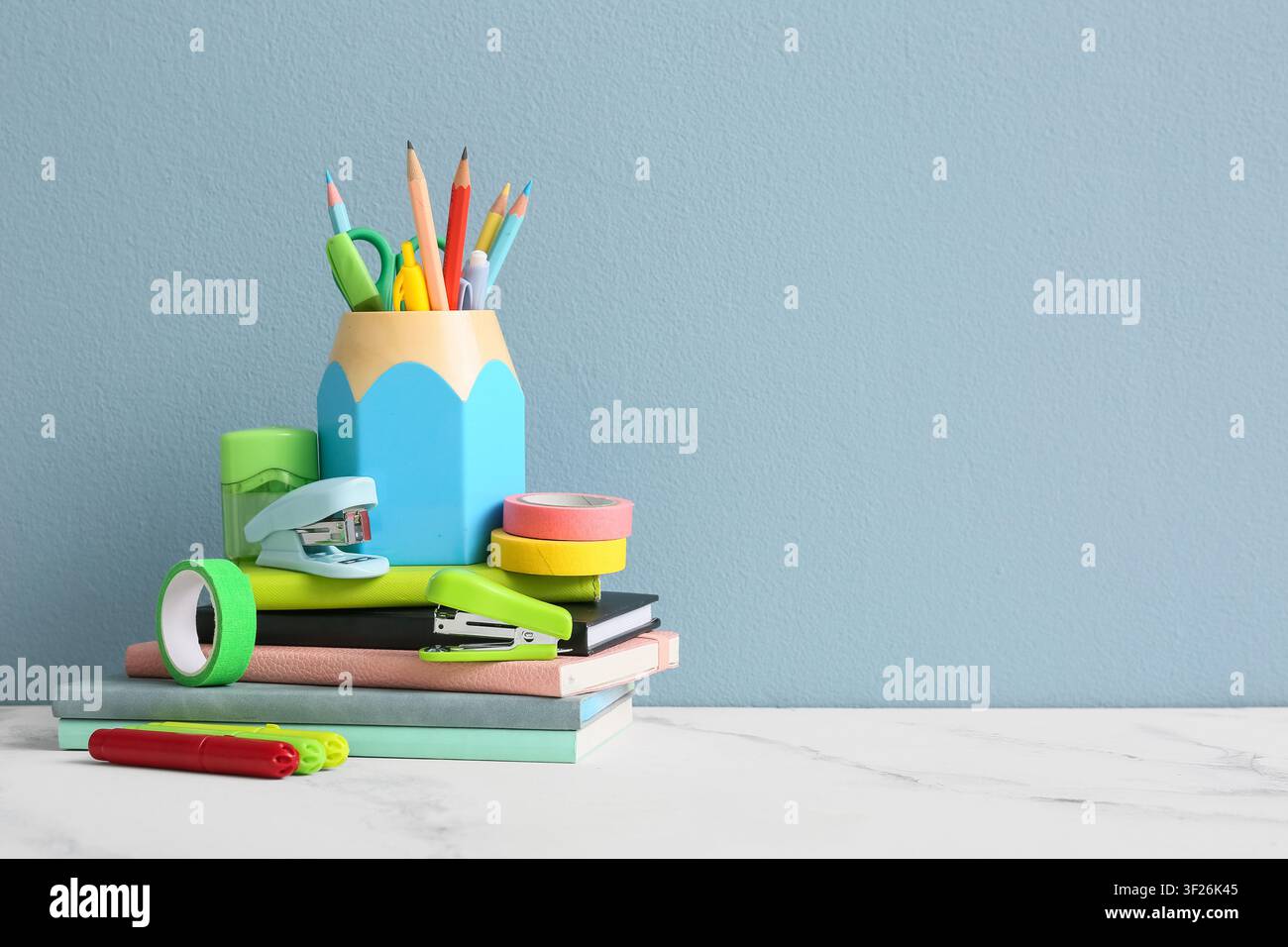 Colorful school supplies and stationery items stacked on books against a light blue background education and learning, the collection includes pencils Stock Photo
