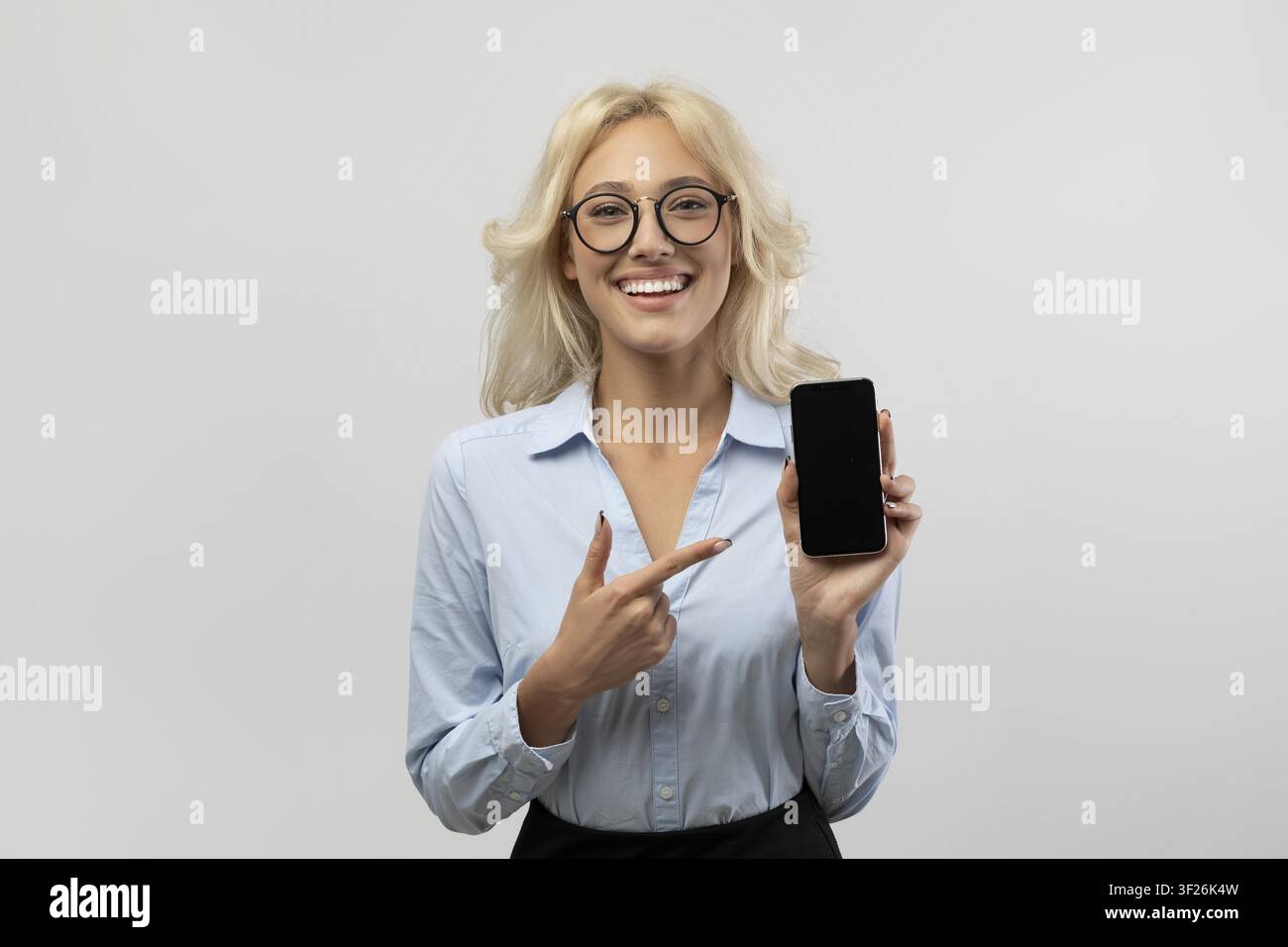 Smiling Young Caucasian Woman Pointing At Smartphone In Office, Business Concept Stock Photo
