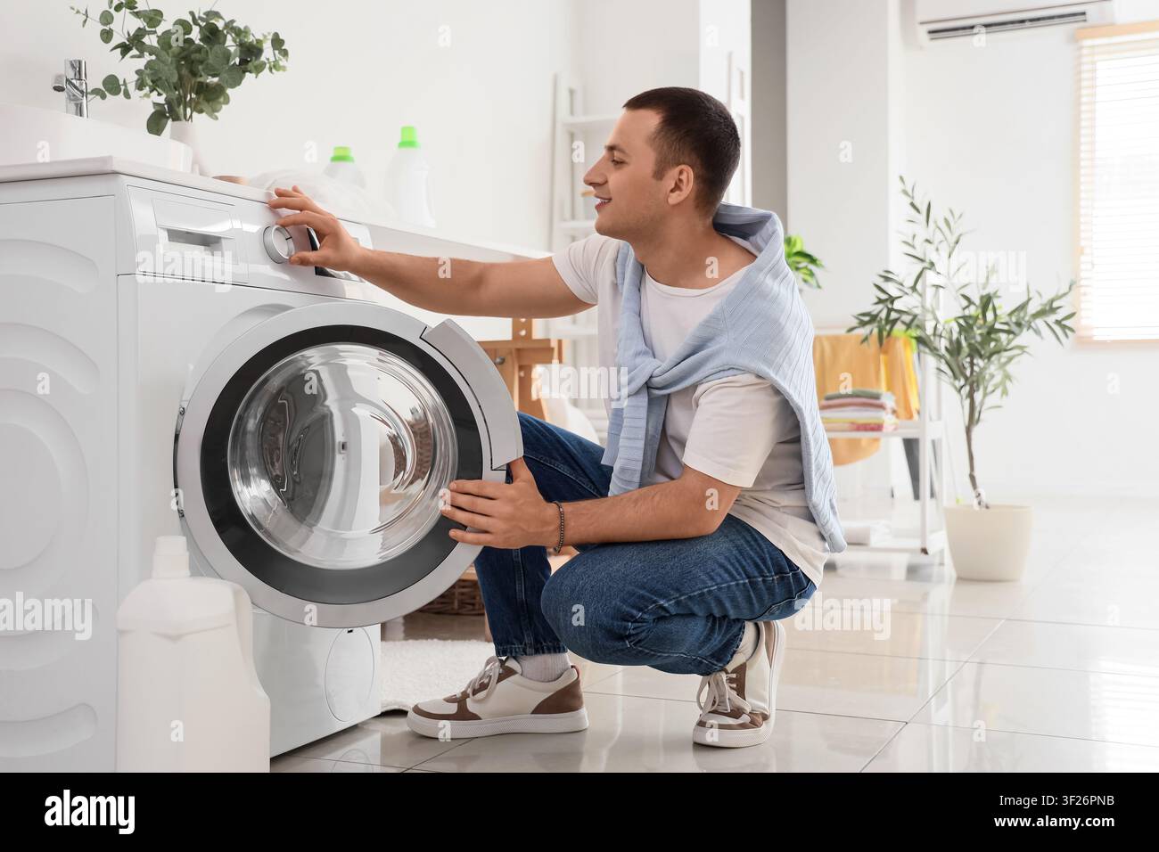Young man using washing machine in laundry room Stock Photo