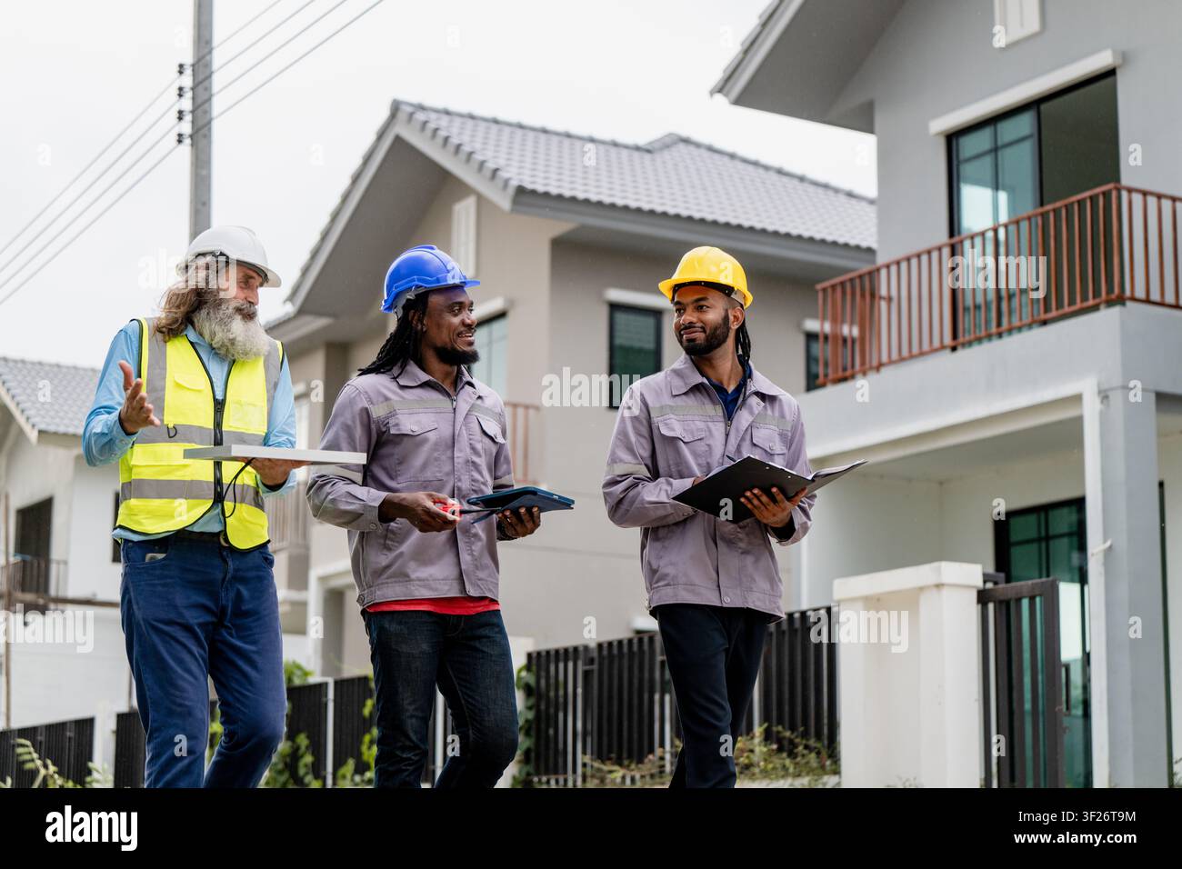 Construction engineers walking through residential development site to inspect and coordinate building progress, discussing work progress while walkin Stock Photo
