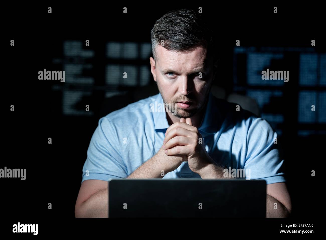 Hacker works on laptop at night. Hacker analyzes code screen in dark room. Hacker monitors network for cyber attack. Hacker targets data system with Stock Photo