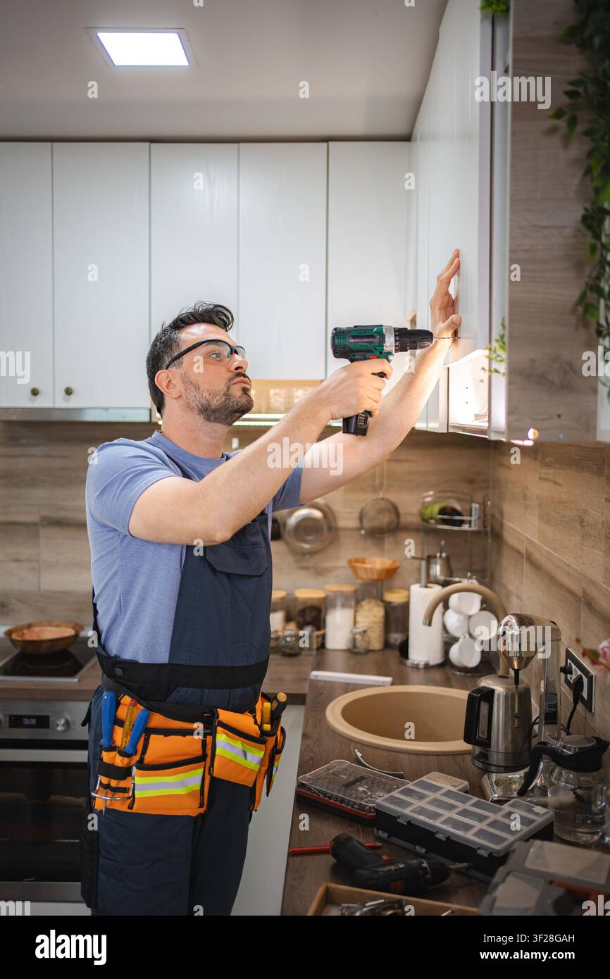 Handyman using cordless screwdriver while installing kitchen cabinets Stock Photo