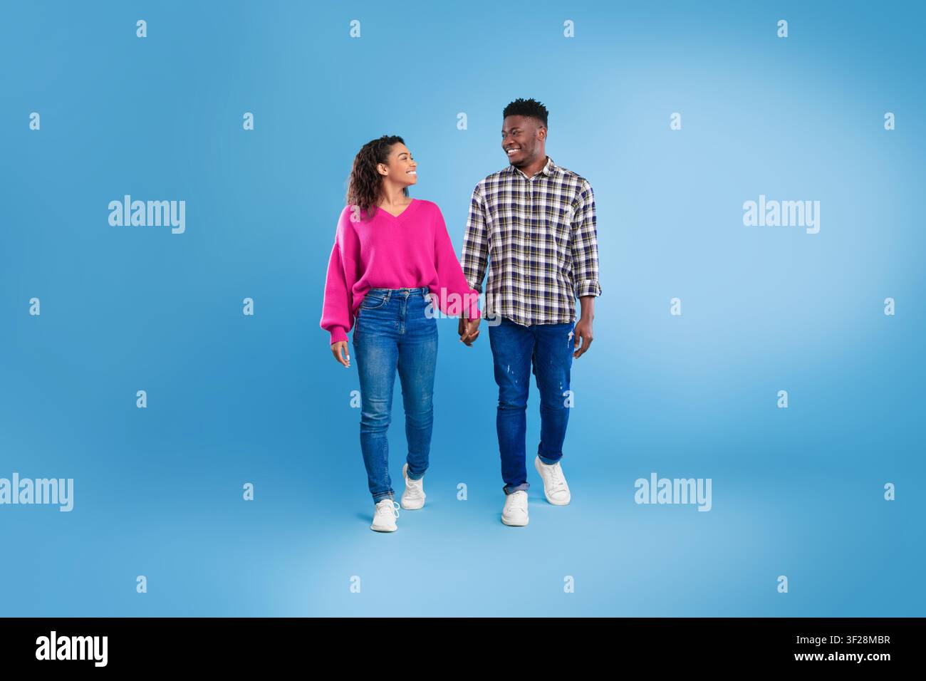 Happy Young Couple Holding Hands And Smiling Walking On Blue Background Stock Photo