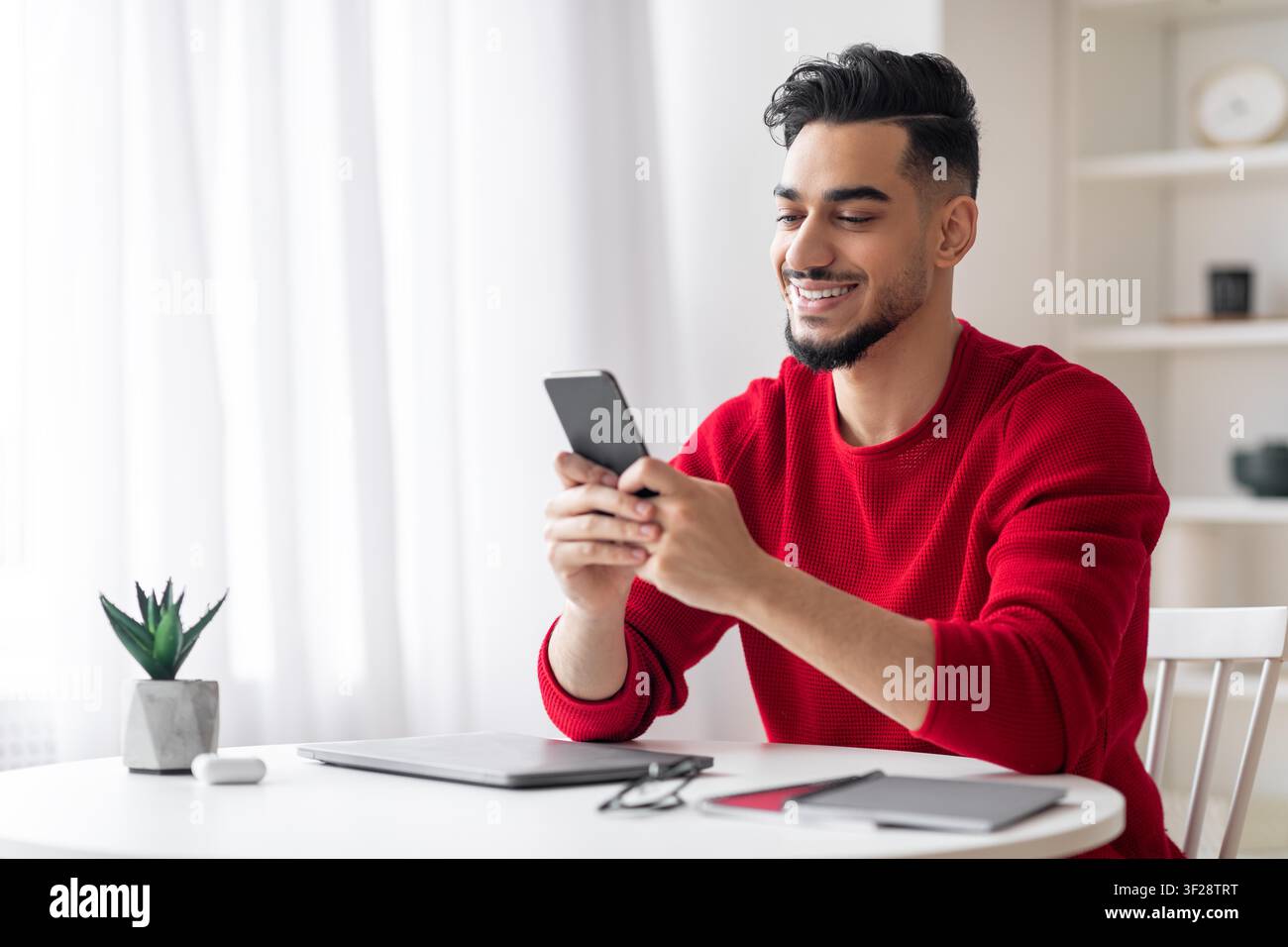 Smiling Young Middle Eastern Man Using Smartphone At Home Office, Business Concept Stock Photo