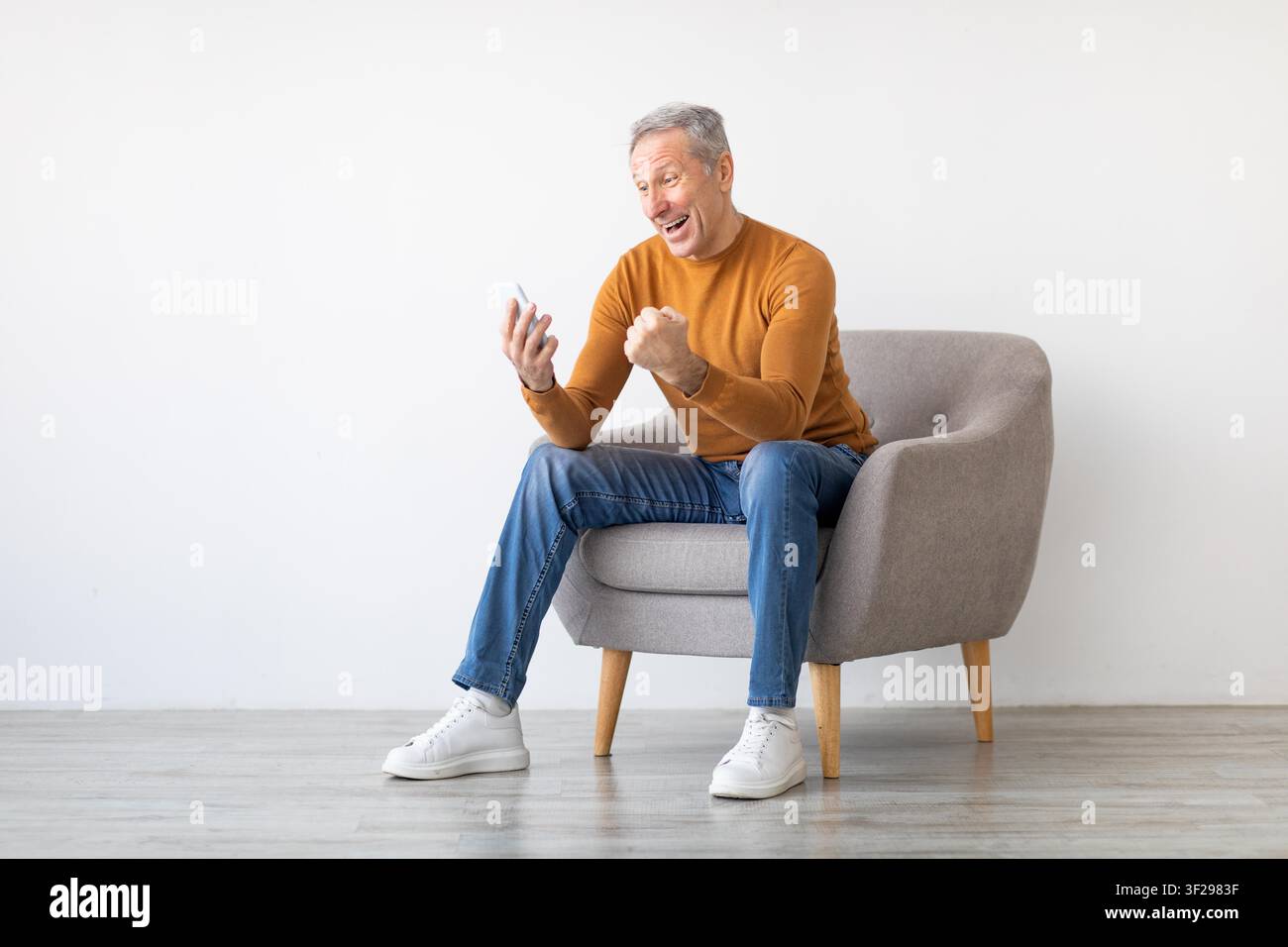 Happy Elderly Caucasian Man Celebrating Positive News While Using Smartphone, Home Setting Stock Photo