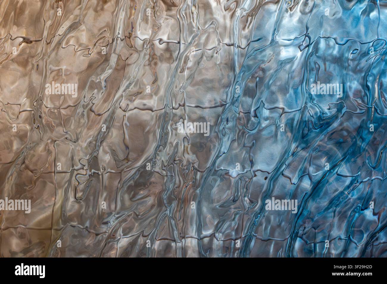 Wavy glass texture in warm gold and cool blue tones, abstract fluid pattern background for design Stock Photo