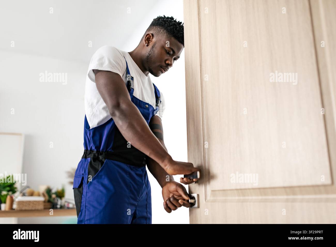 Young Black Man Fixing Door Lock With Focused Expression, Home Interior Setting Stock Photo