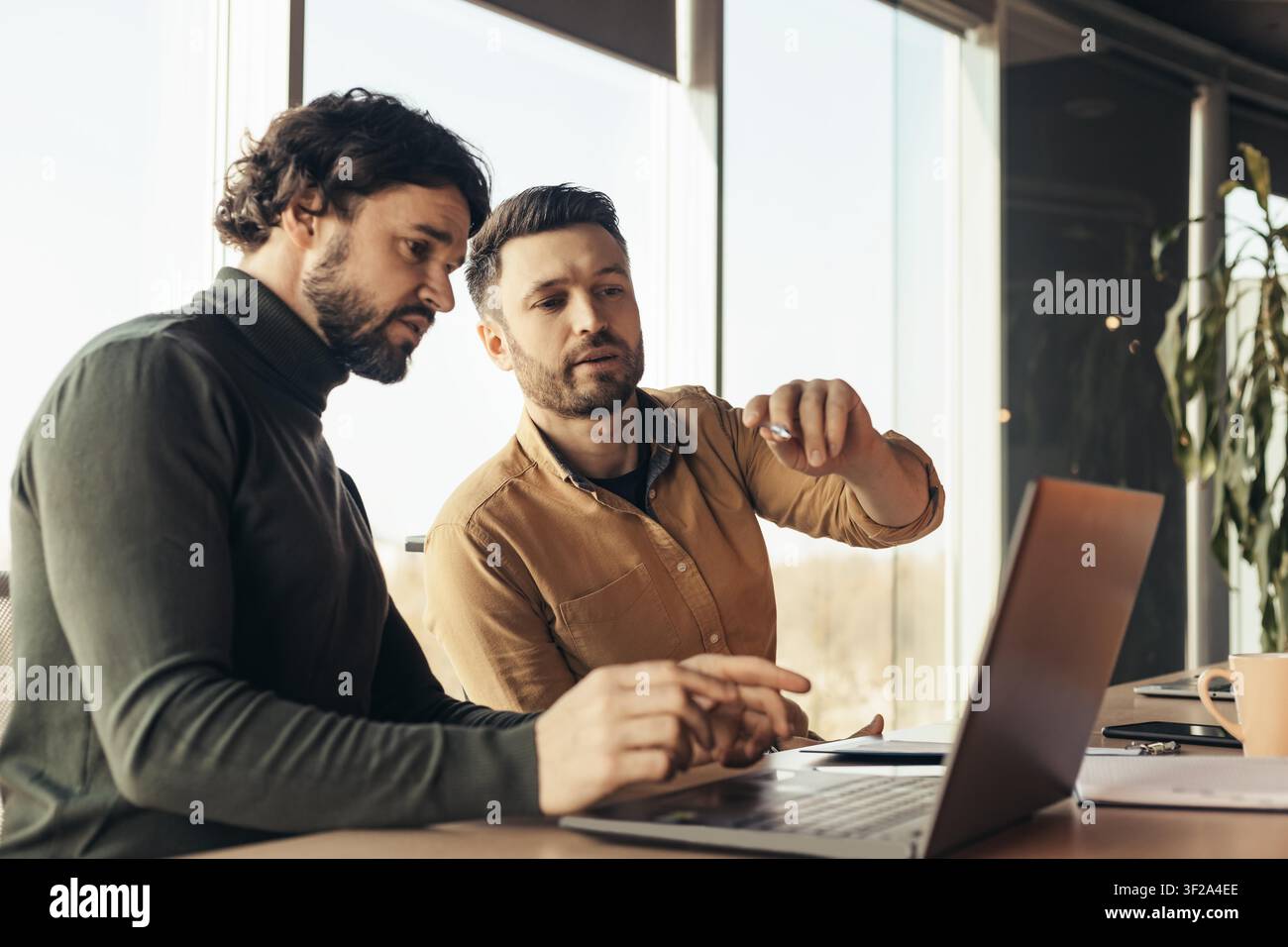 Two Men Collaborating At Office Computer, Focused On Work, Business Concept Stock Photo