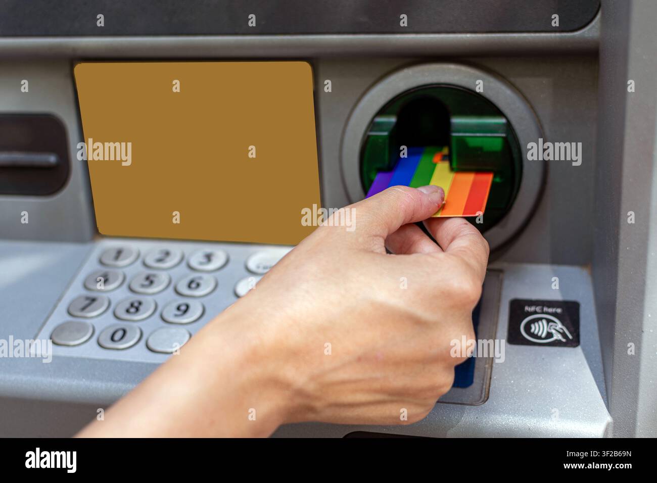 Hand inserting rainbow credit card into atm machine Stock Photo