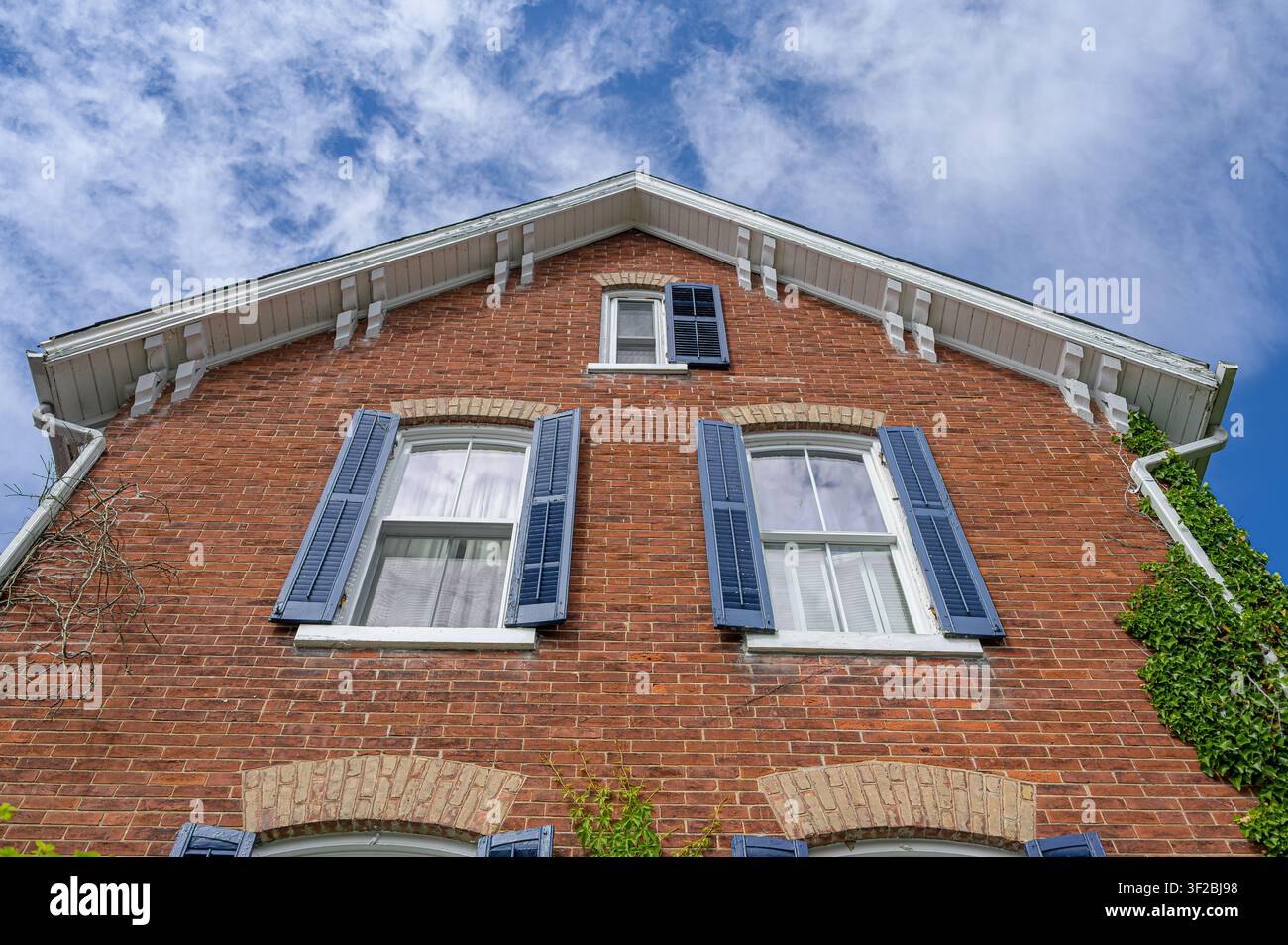 Red brick facade with blue shutters viewed from a dramatic low-angle perspective. Stock Photo