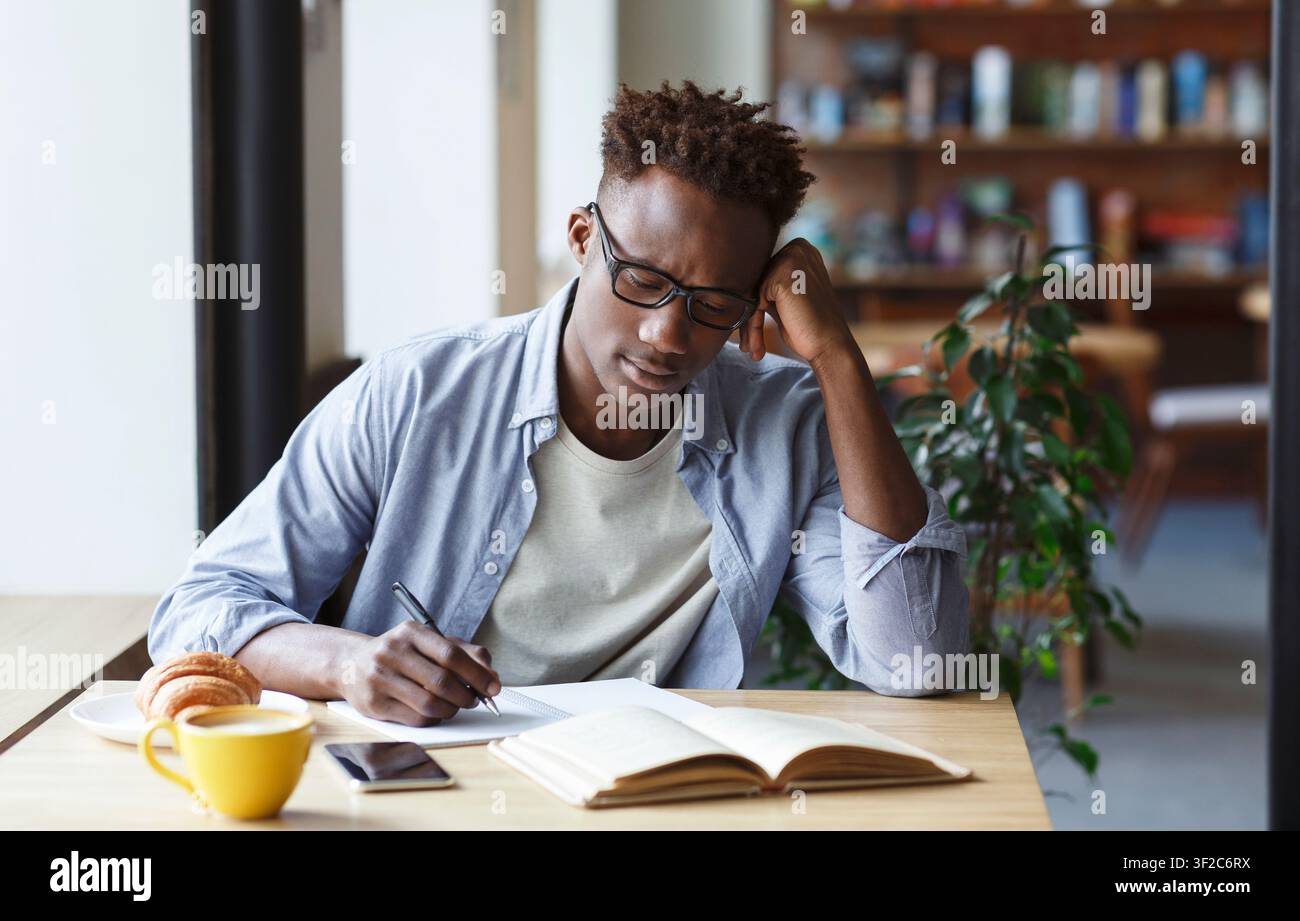 Focused African American student taking notes from book in cafe Stock Photo