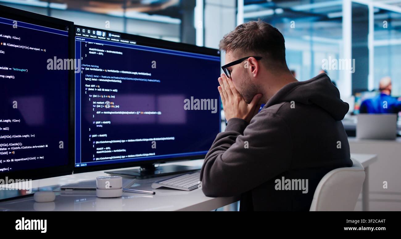 Tired Software Engineer Struggles With Coding Tasks At His Office Desk. Stock Photo
