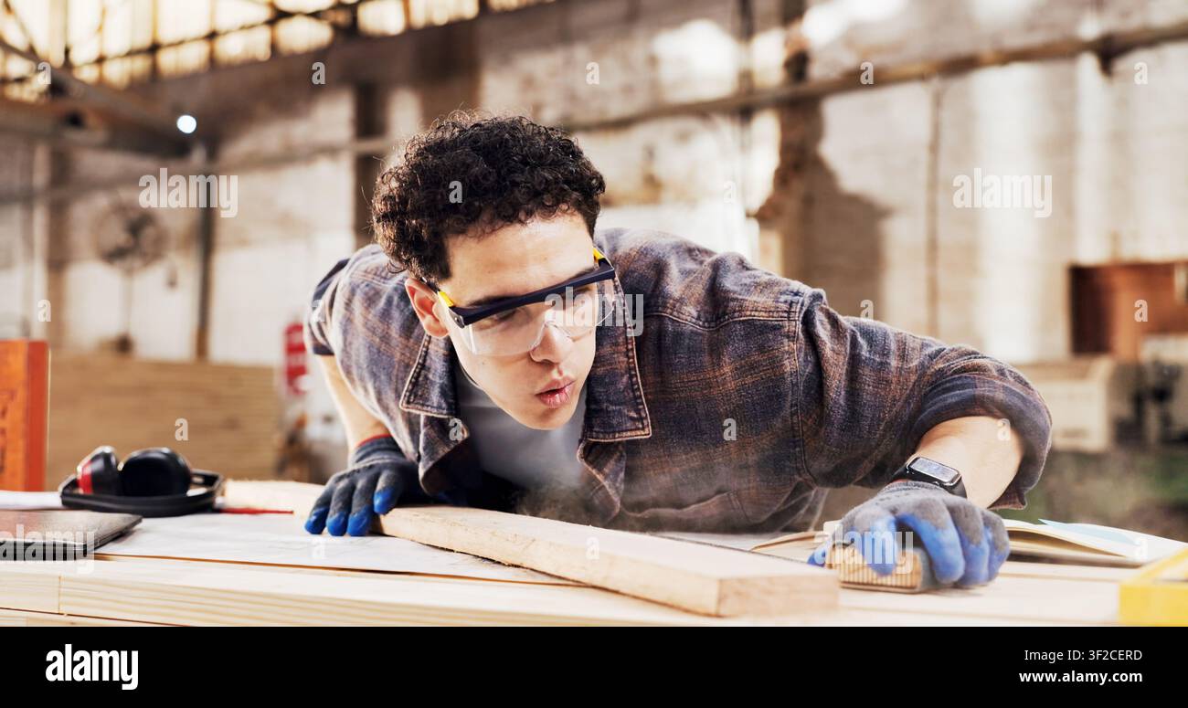 Carpenter, sanding and man blow dust in workshop with wood for clean, productivity or production. Person, safety gear and warehouse with tools for Stock Photo