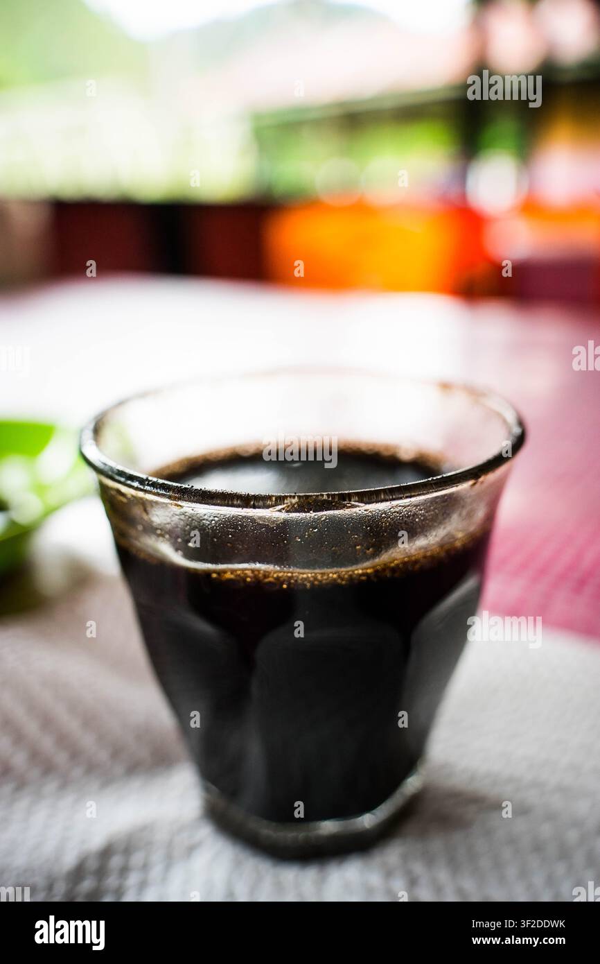 Glass cup of fresh black coffee sitting on a red checkered tablecloth at an outdoor cafe table Stock Photo