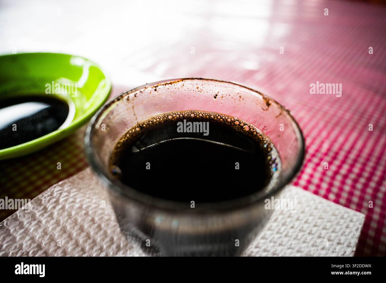 Glass cup of fresh black coffee sitting on a red checkered tablecloth at an outdoor cafe table Stock Photo