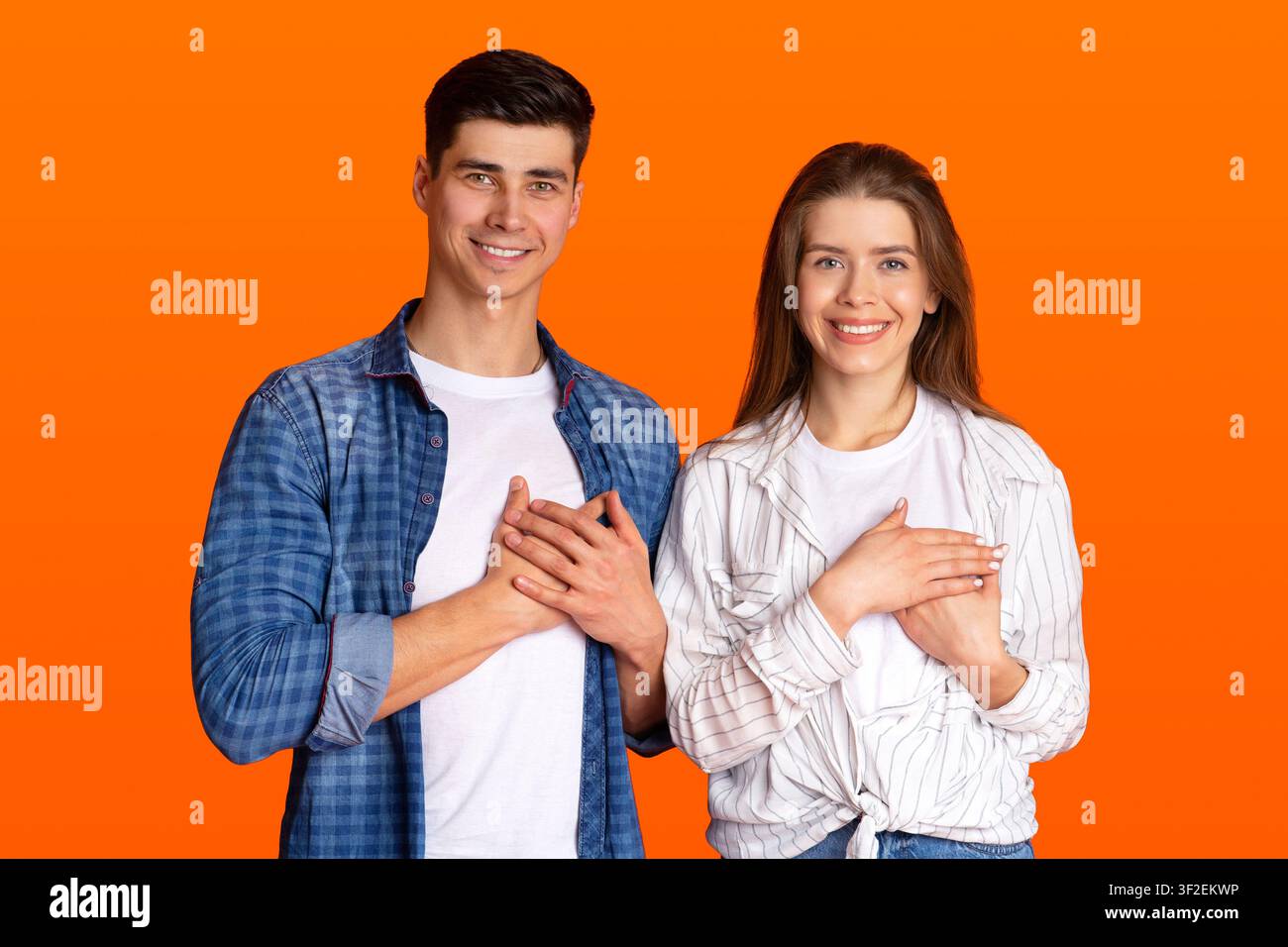 Grateful gesture concept. Pretty smiling young male and female in casual clothes keep hands on chest, being thankful Stock Photo