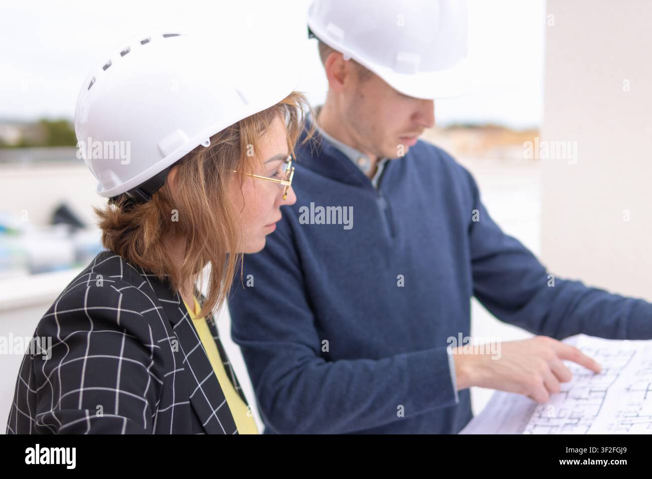 Engineering professionals collaborating on construction blueprints and architectural plans, discussing design details and project specifications while Stock Photo