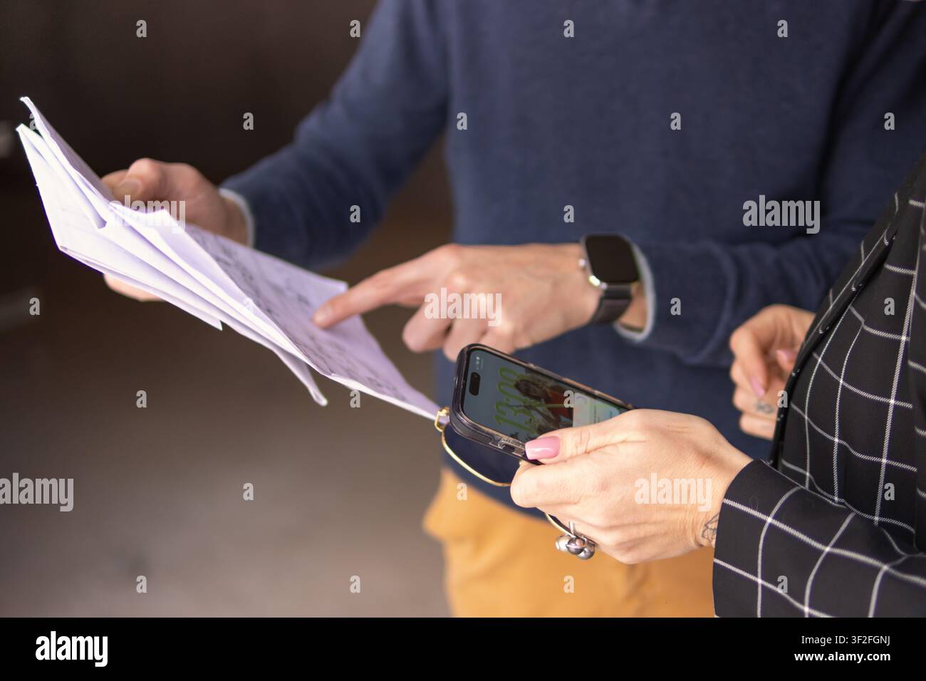 Professionals discussing project plans, analyzing paperwork and information on a smartphone, connecting traditional documents with digital data for st Stock Photo
