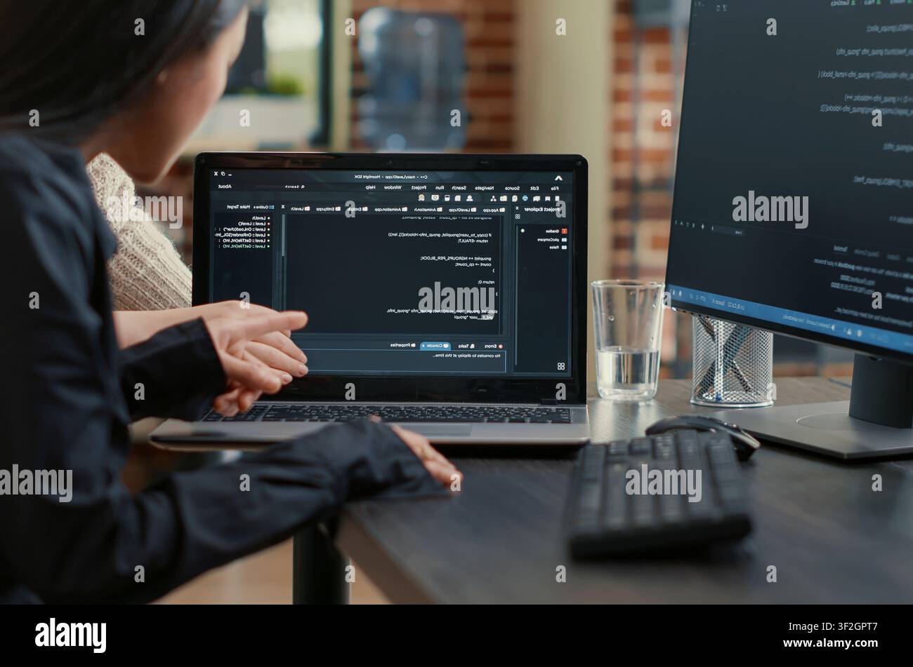 Programming team reviews an algorithm on a laptop screen, pointing at source code while collaborating on a data coding project at the desk. Stock Photo