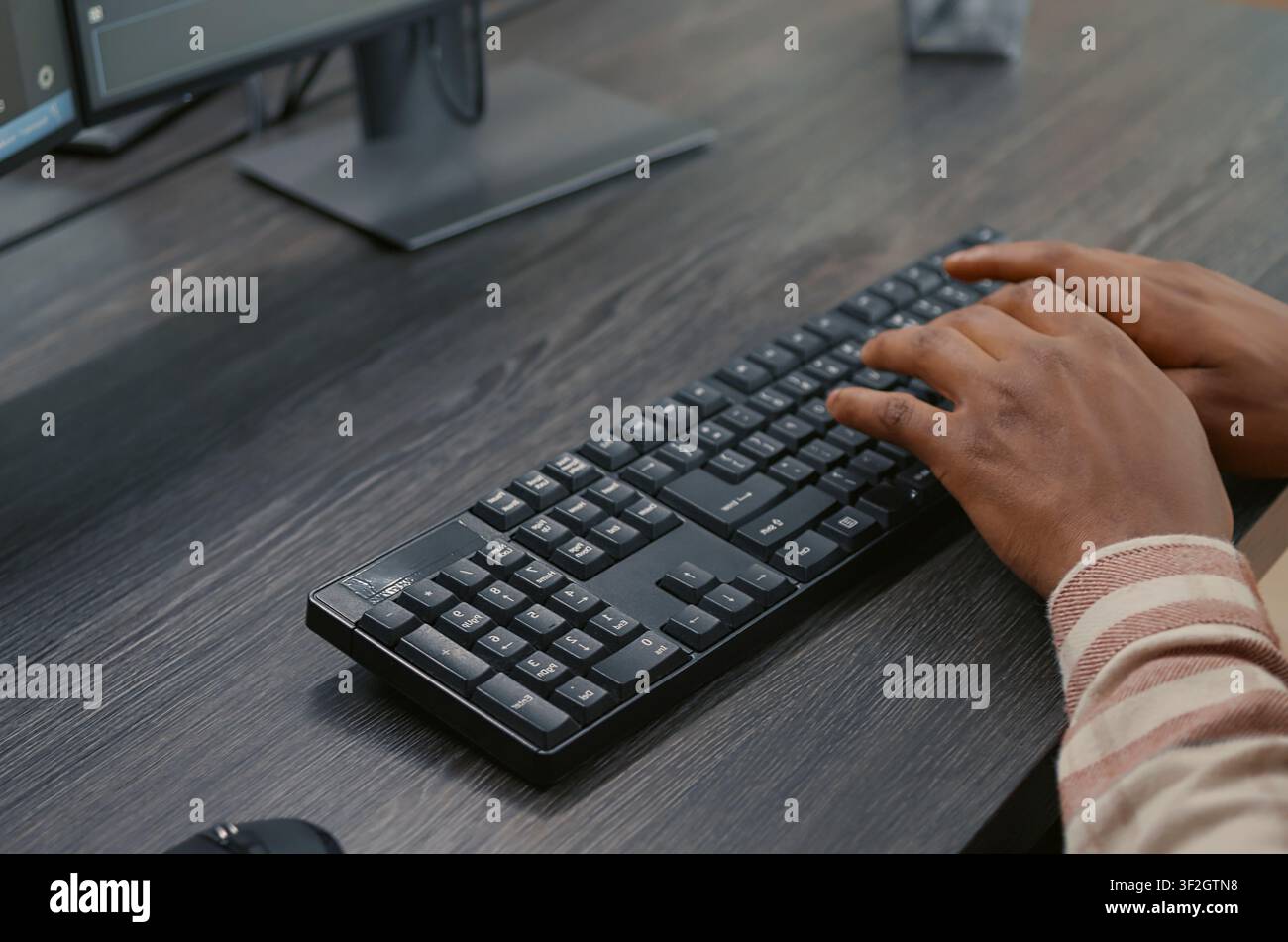 African American programmer types on a keyboard while viewing programming interfaces on multiple screens, developing algorithms as a system engineer at a desk. Stock Photo