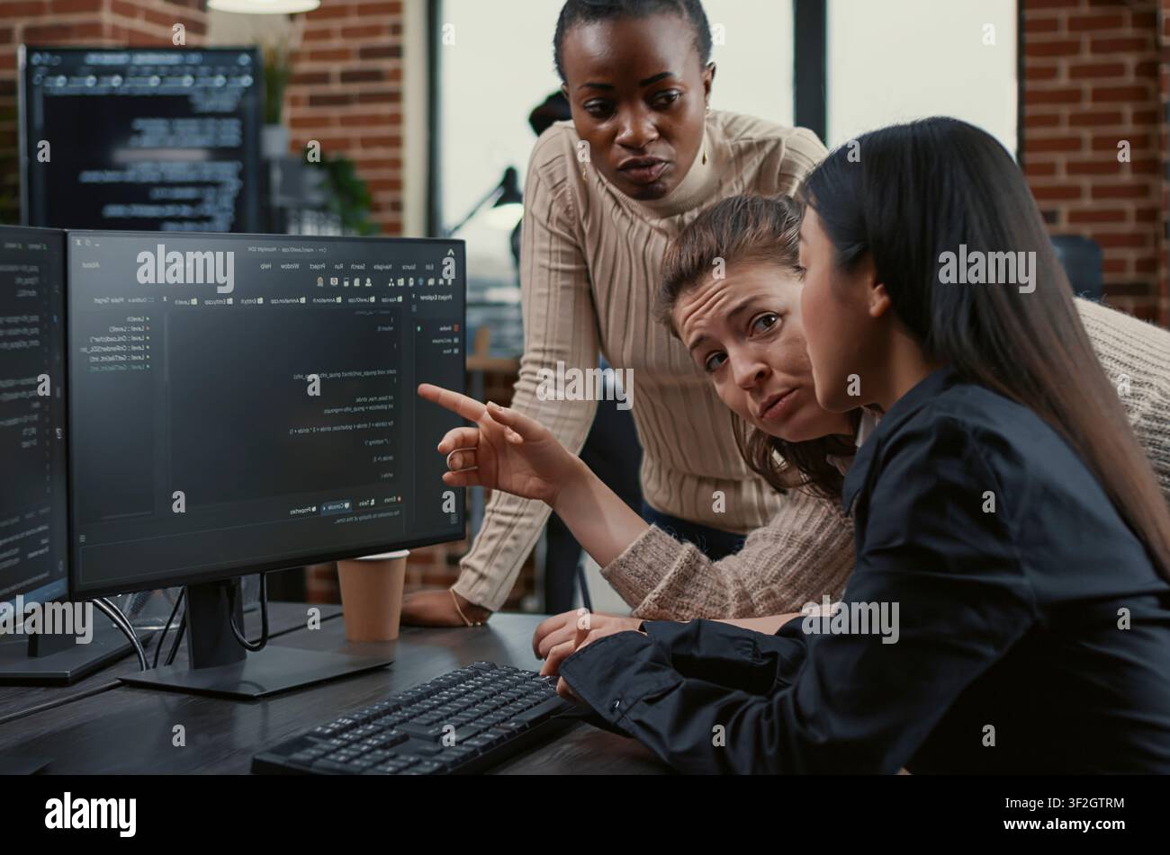 Programmer points at a computer screen to explain running code while coworkers brainstorm software ideas, collaborating on an IT group project in a freelance agency. Stock Photo