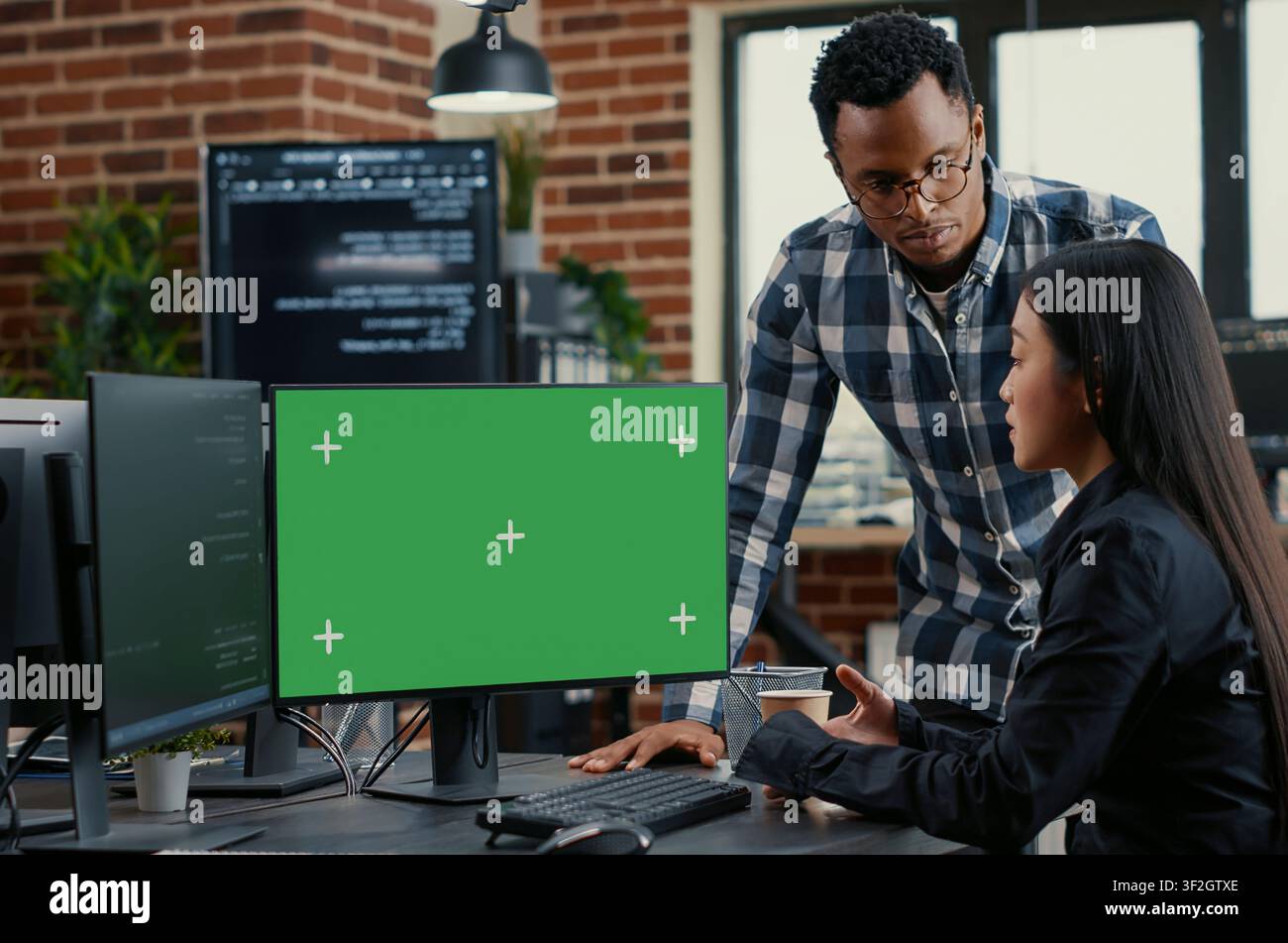 Mixed programmers analyze source code beside a green screen chroma key mockup, discussing algorithms, app development and online cloud computing in a server room. Stock Photo