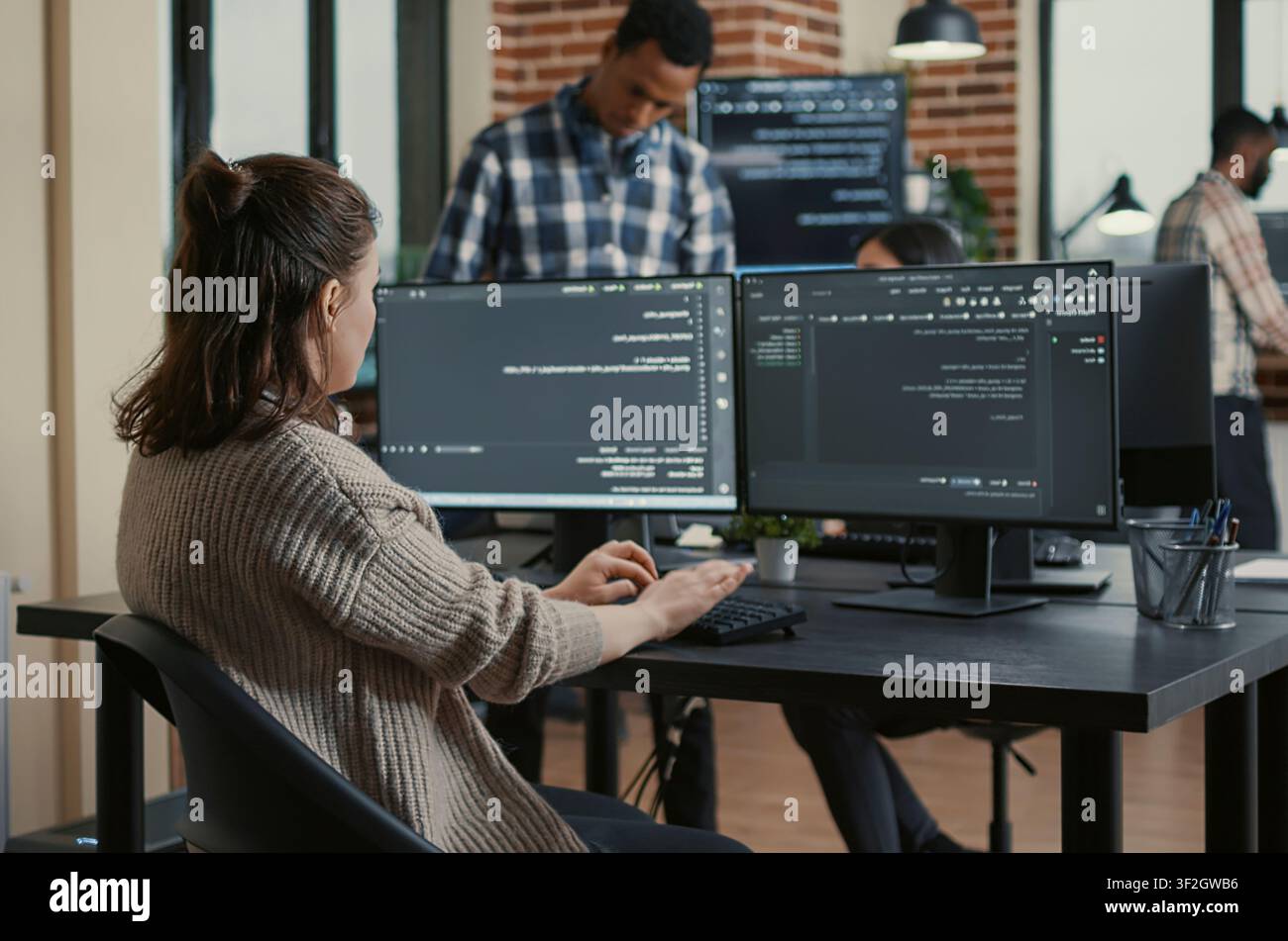 Concentrated software developer coding software reviewing multiple computer screens around computer screens, showing developer teamwork, source code discussion and cloud programming workflow. Stock Photo