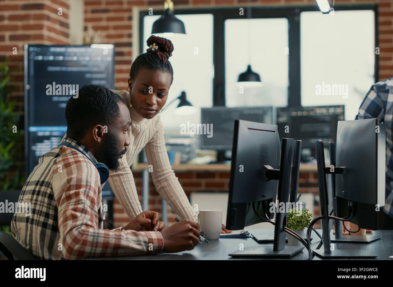 Collaborative team reviews cloud interface code around computer screens, showing developer teamwork, source code discussion and cloud programming workflow. Stock Photo