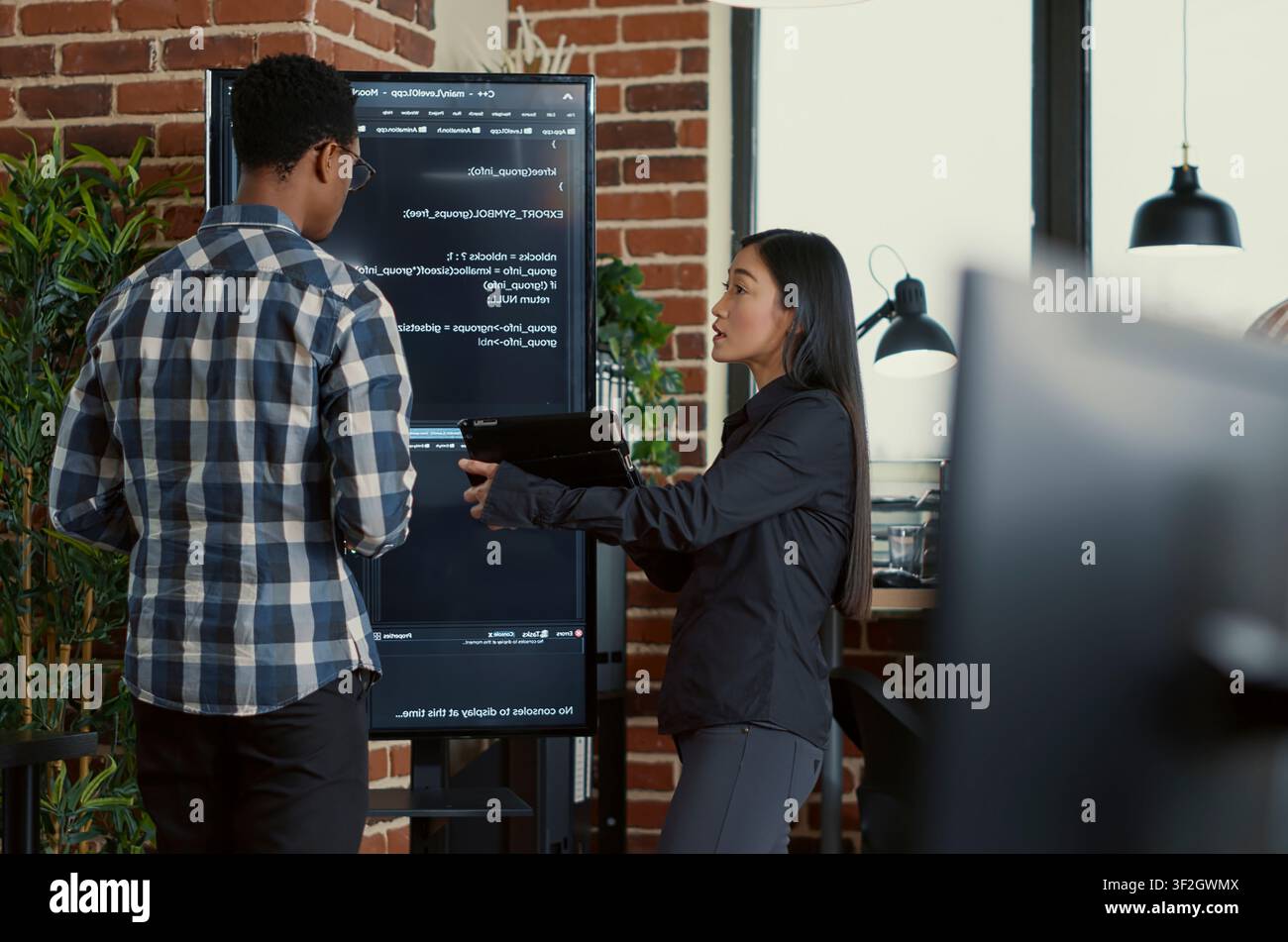 Team of coders analyzes code errors on a wall screen while using a digital tablet beside a programmer working with neural network software. Stock Photo
