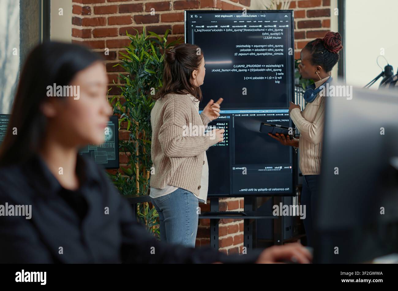 System engineers compare source code errors on a wall screen using a digital tablet while a programmer writes algorithm code during a debugging review. Stock Photo