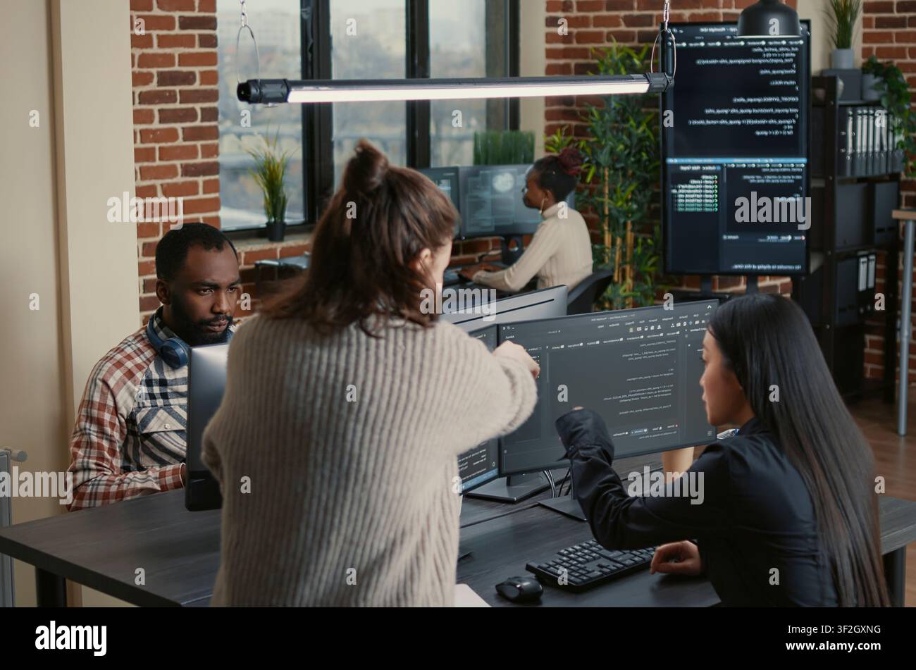 Software programmer pointing pencil at source code on computer screen explaining algorithm to coworker standing next to desk around computer screens, showing developer teamwork, source code. Stock Photo